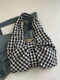 Black and white checked bow shoulder bag resting against denim on a chair.