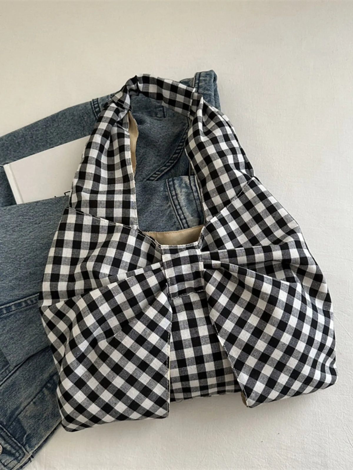 Black and white checked bow shoulder bag resting against denim on a chair.