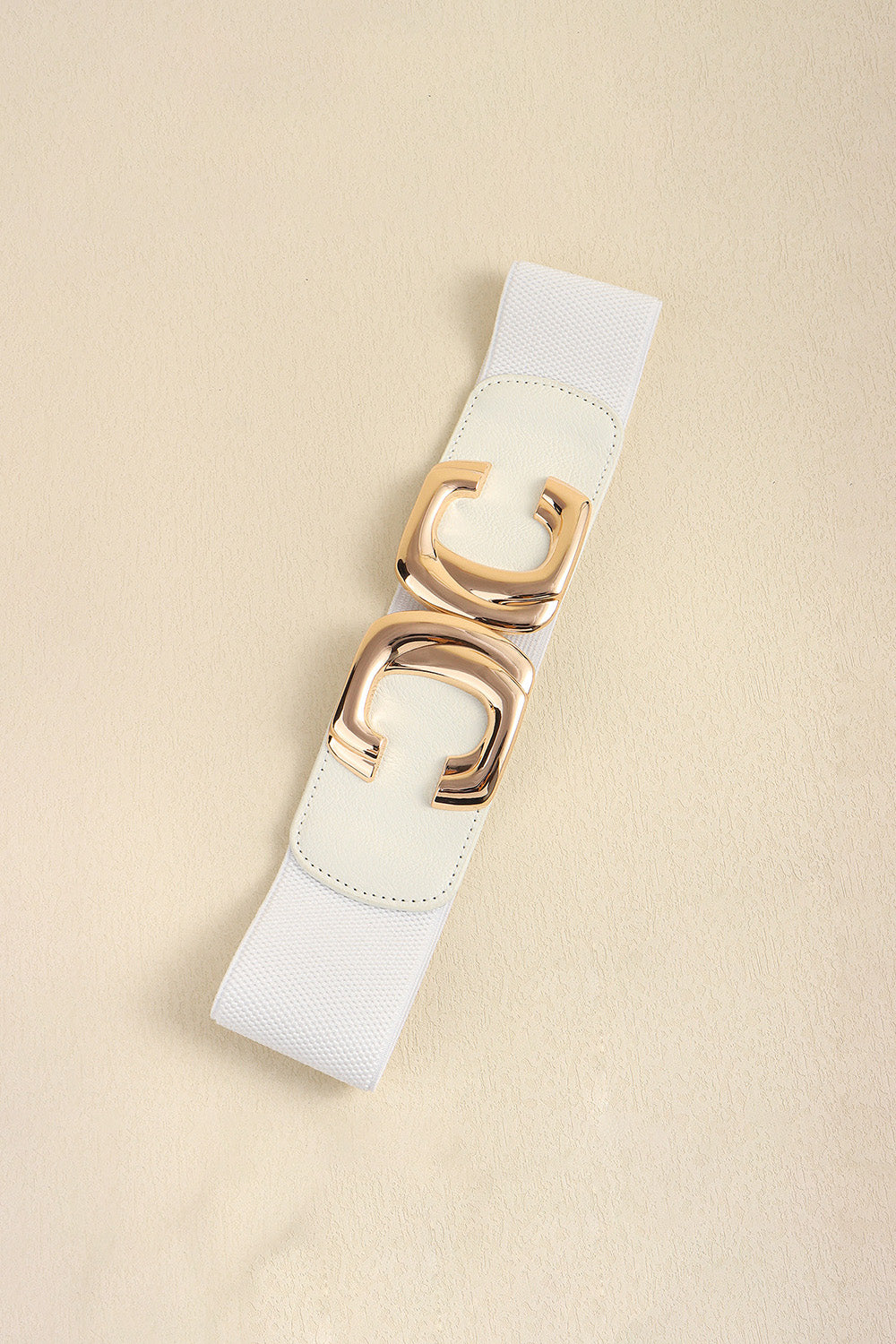 White waist belt laid diagonally with the metal buckle fastened.