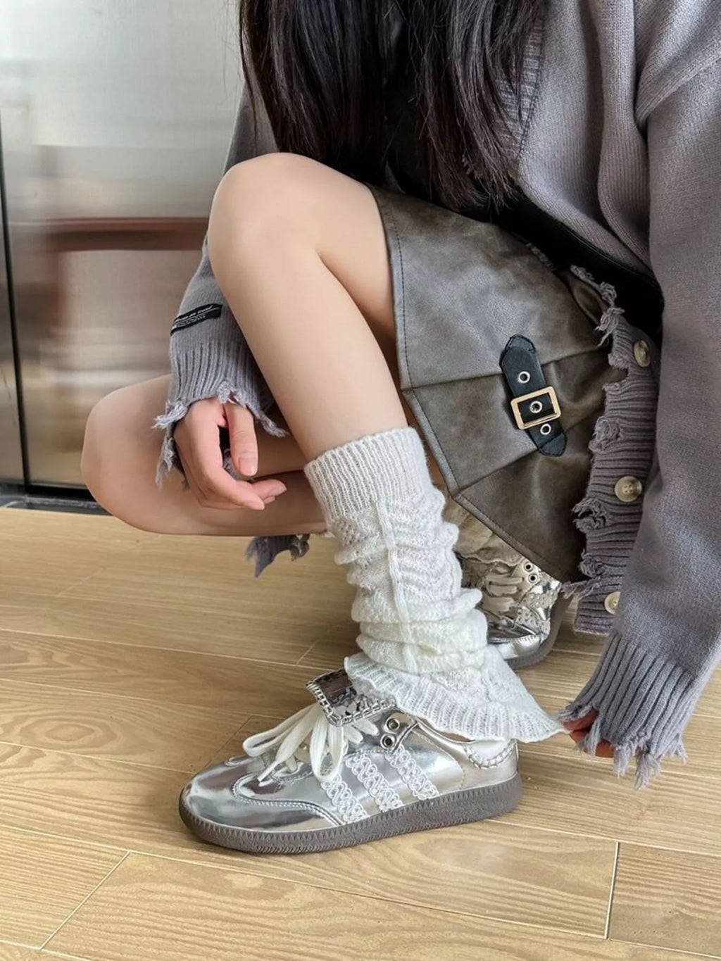 Close-up of a white leg warmer being adjusted above a silver sneaker.