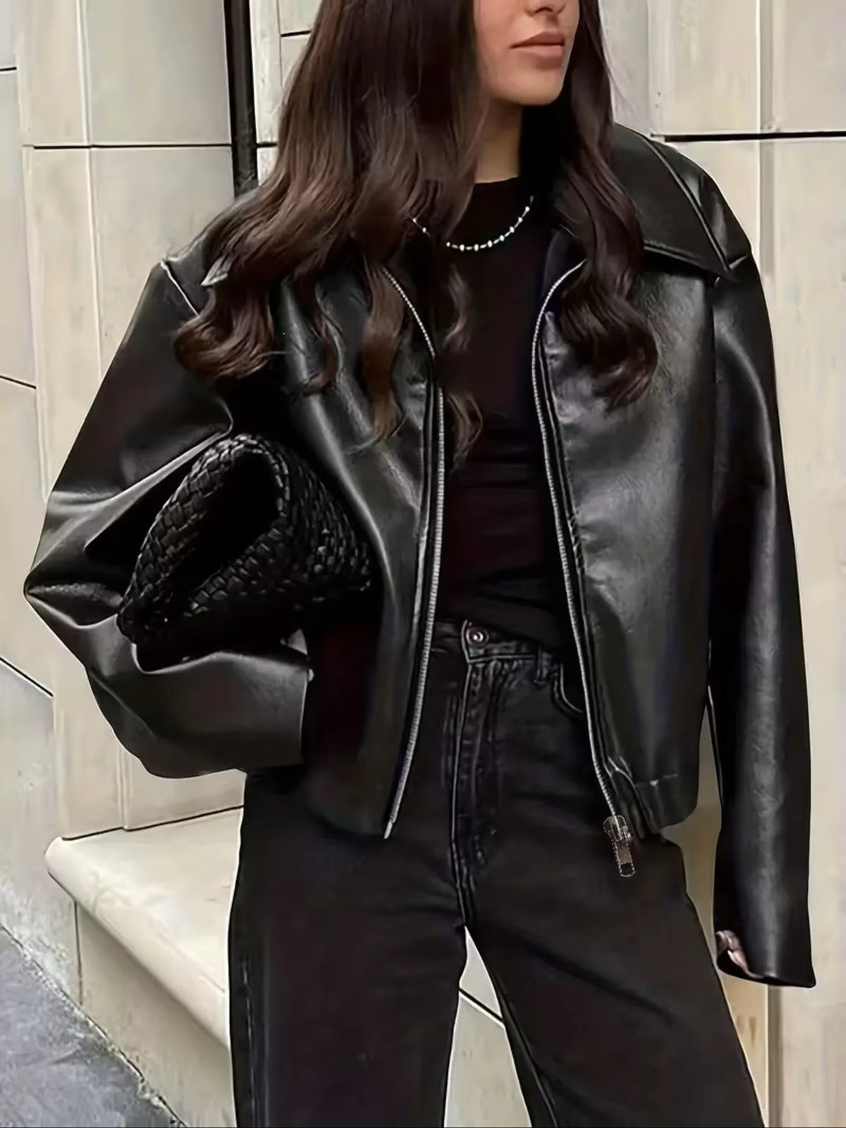 Black faux leather moto jacket worn open with black jeans and a black top.