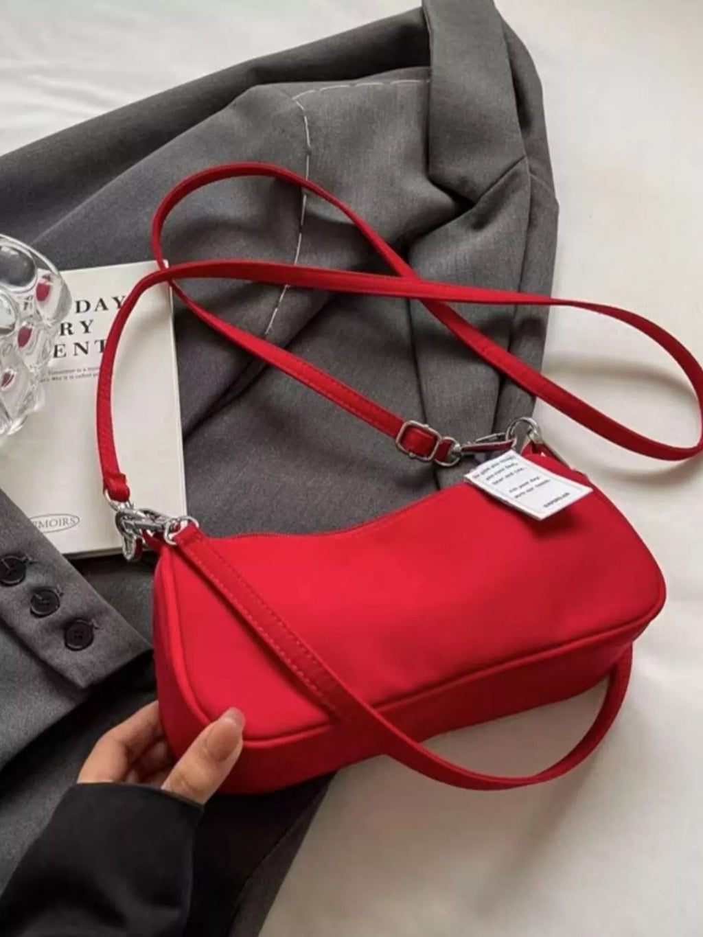 Red crossbody bag turned to show its base, with the long adjustable strap spread across gray fabric.