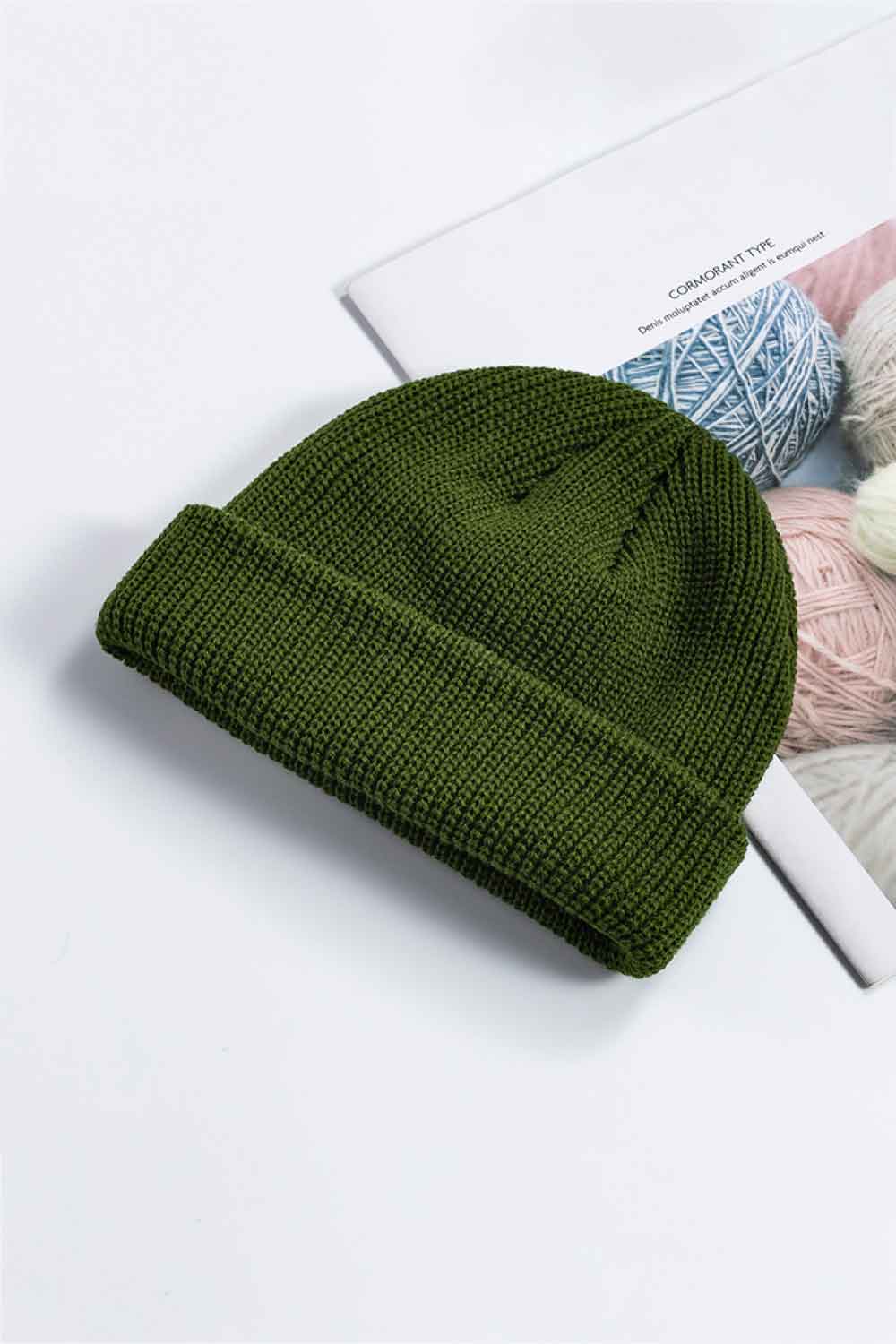 Olive green knit cuff beanie displayed at an angle on a printed page.
