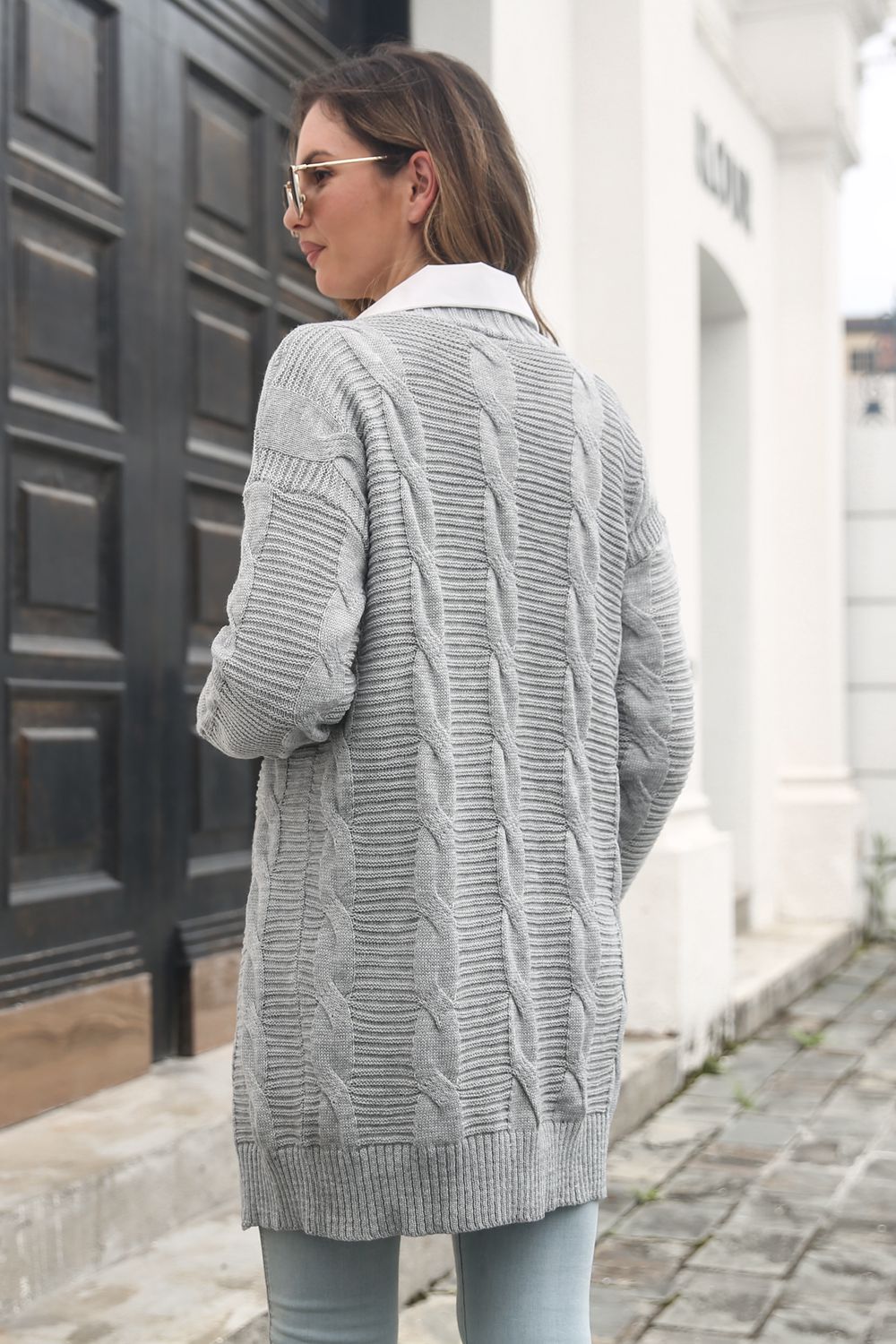Back of the light-gray cardigan showing vertical cable-knit panels and a ribbed hem.
