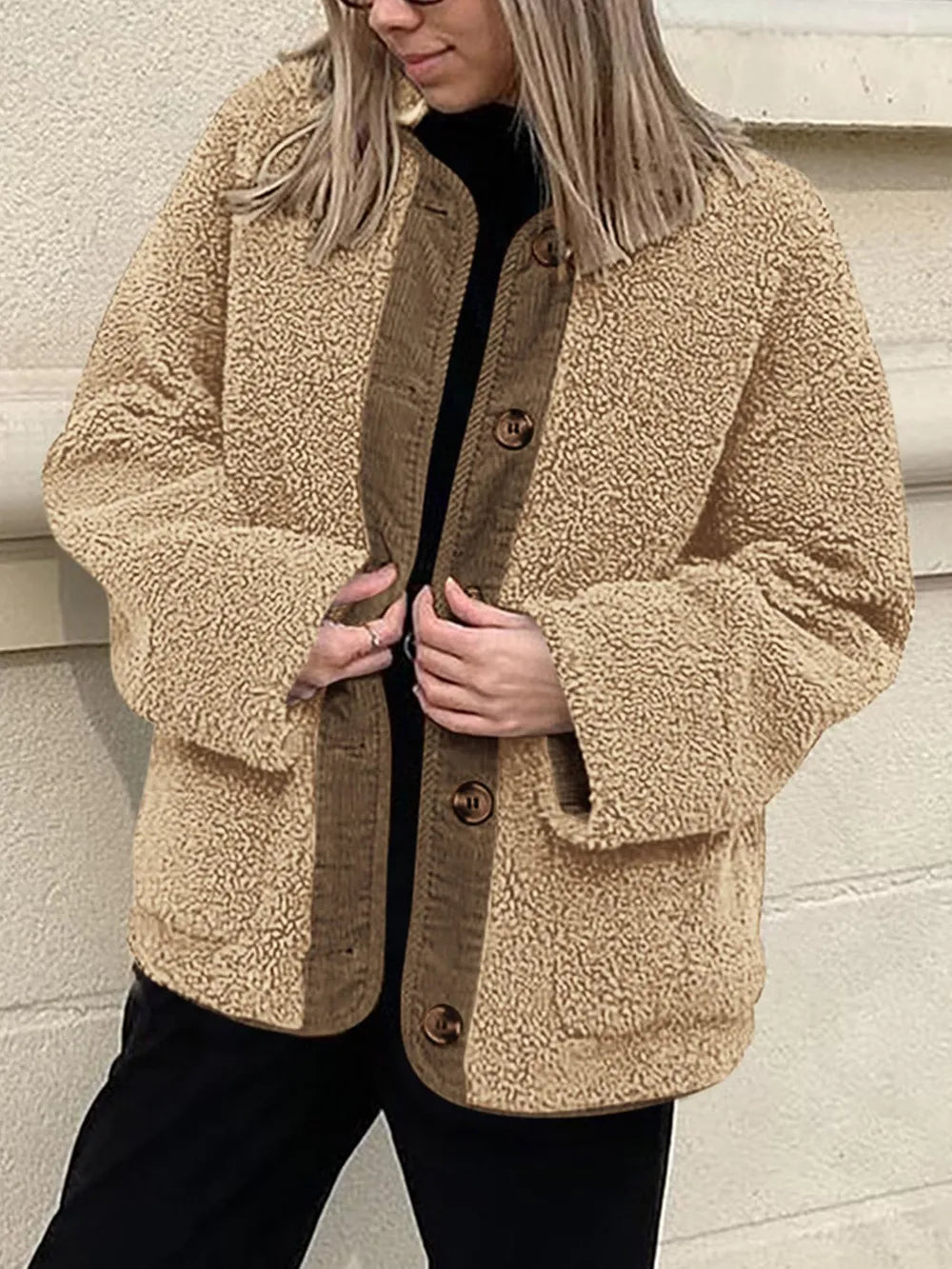 Tan textured jacket held open over a black top and trousers.