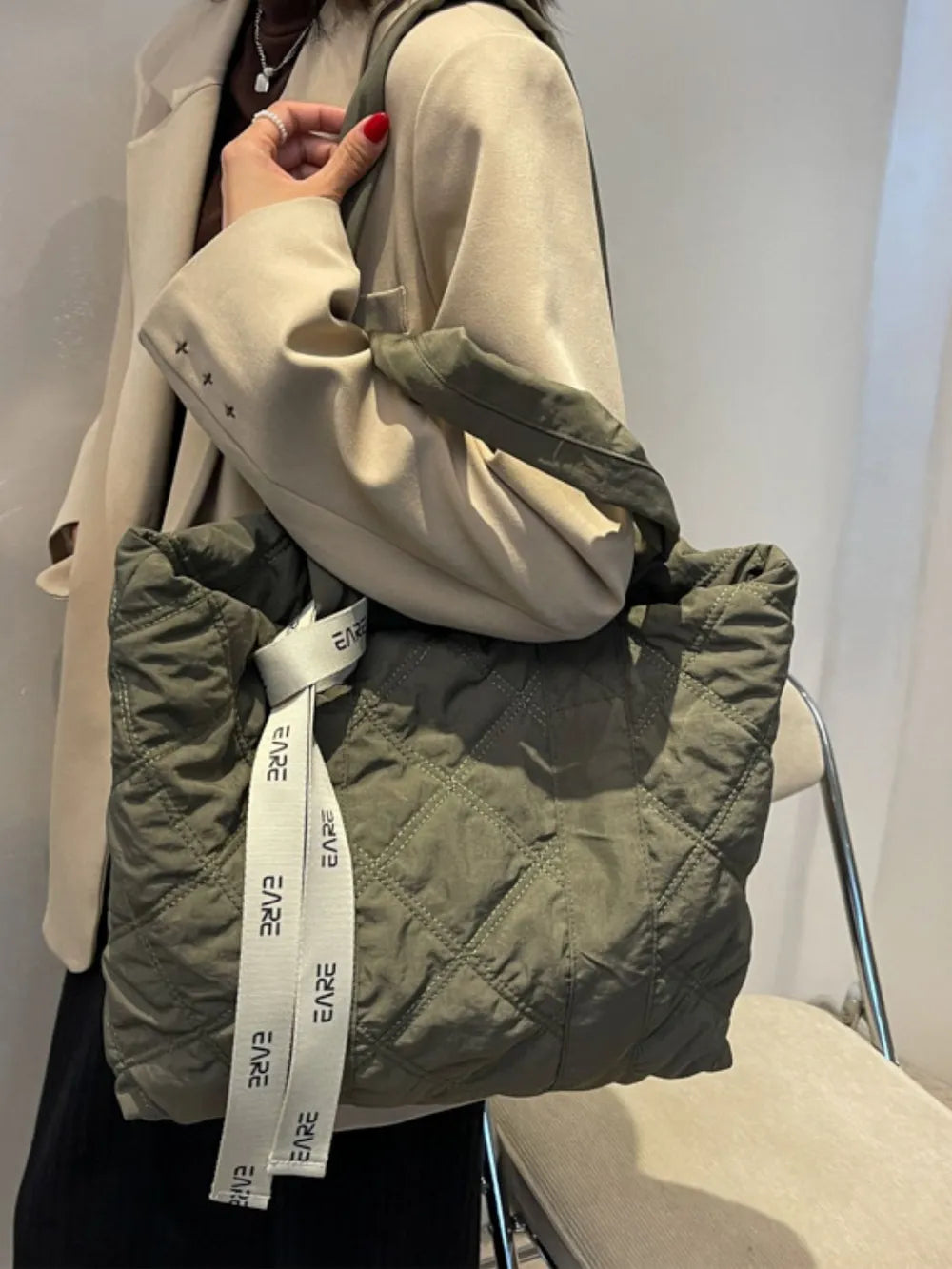 Olive green quilted tote worn on the shoulder with a beige jacket.