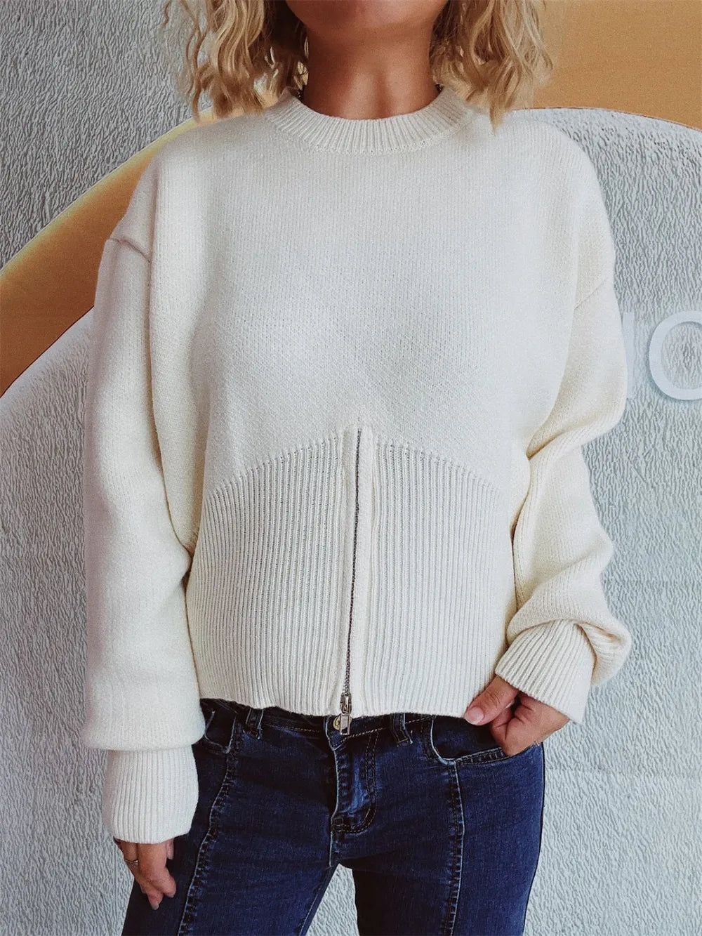 White half-zip knit sweater with the front zip closed, worn with dark jeans.