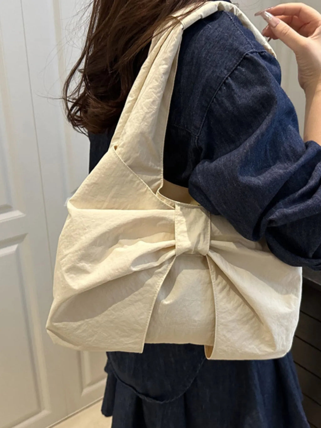 Side view of the cream bow shoulder bag worn with a dark blue outfit.