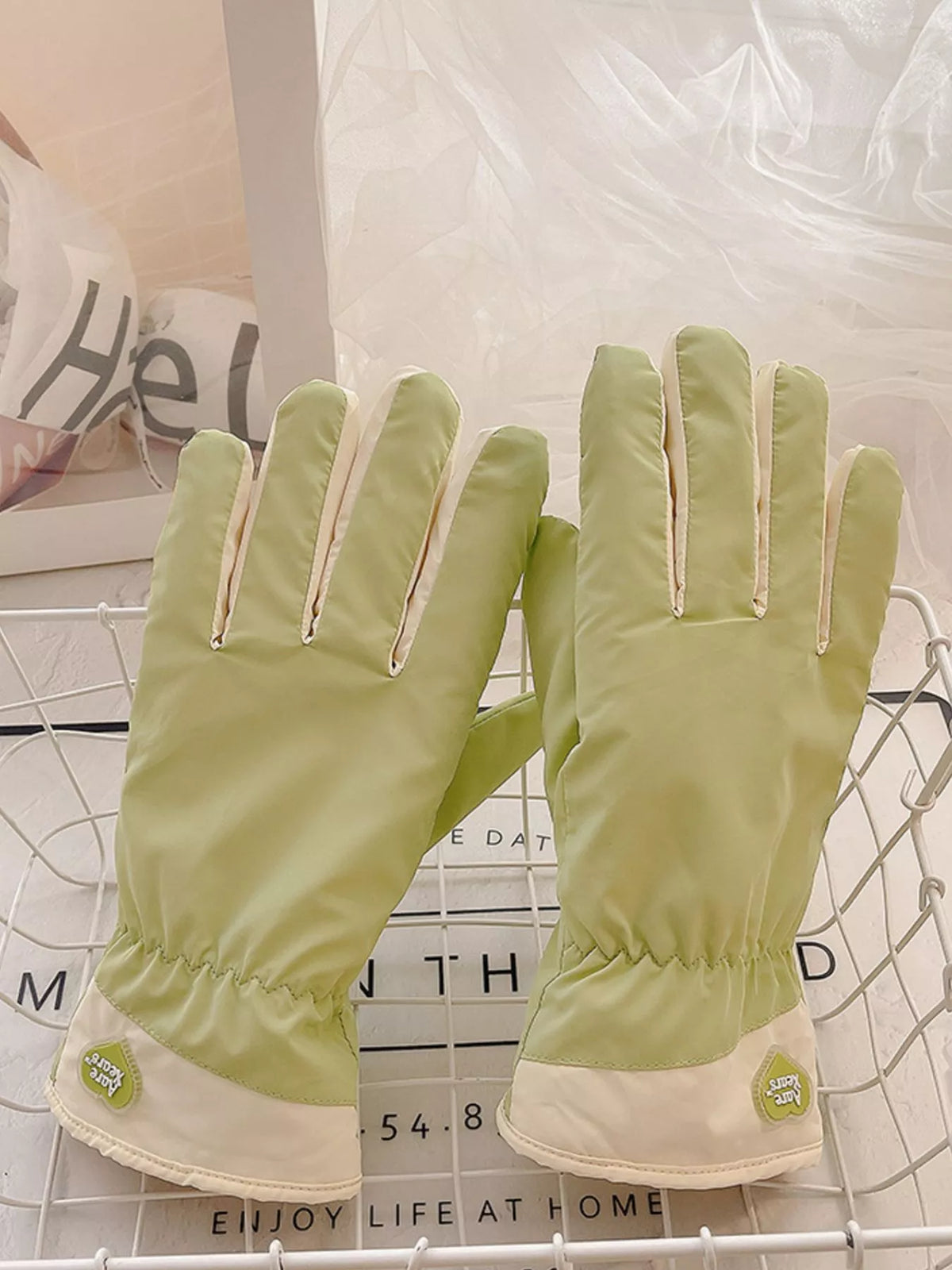 Pair of light green gloves laid side by side with cream cuffs facing down.