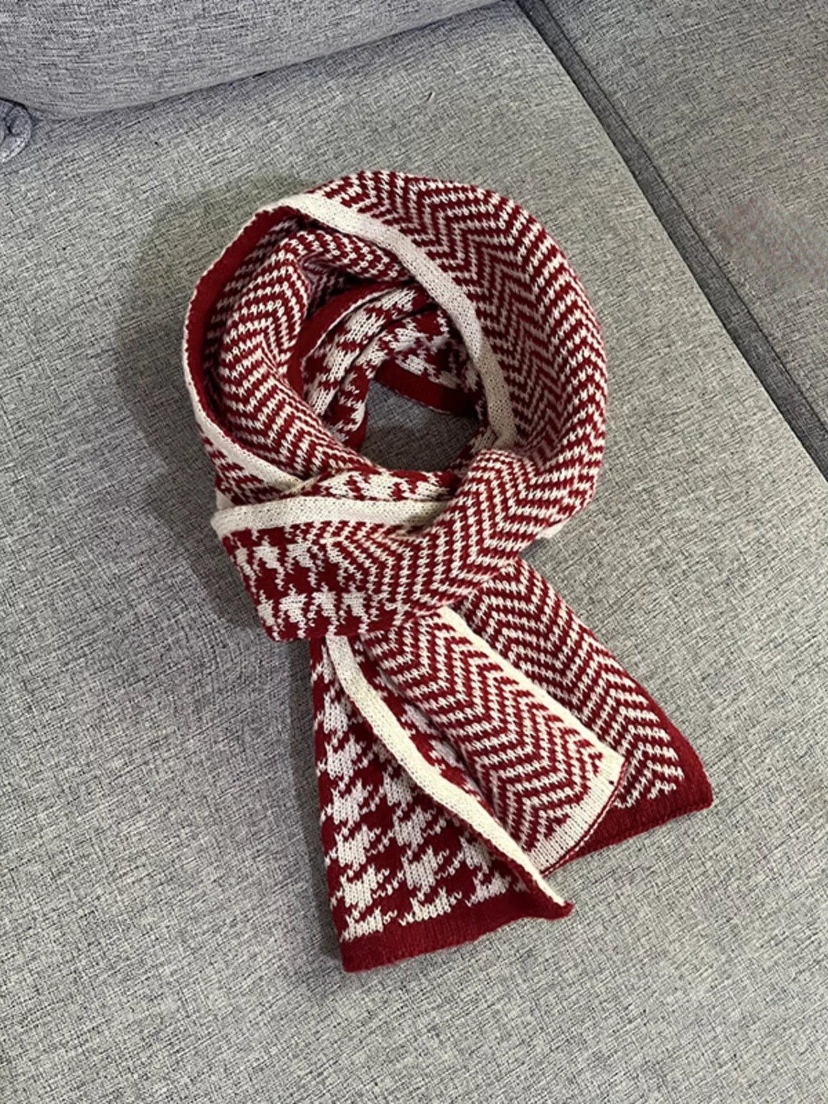 Burgundy houndstooth and chevron scarf looped loosely, laid on a grey couch.