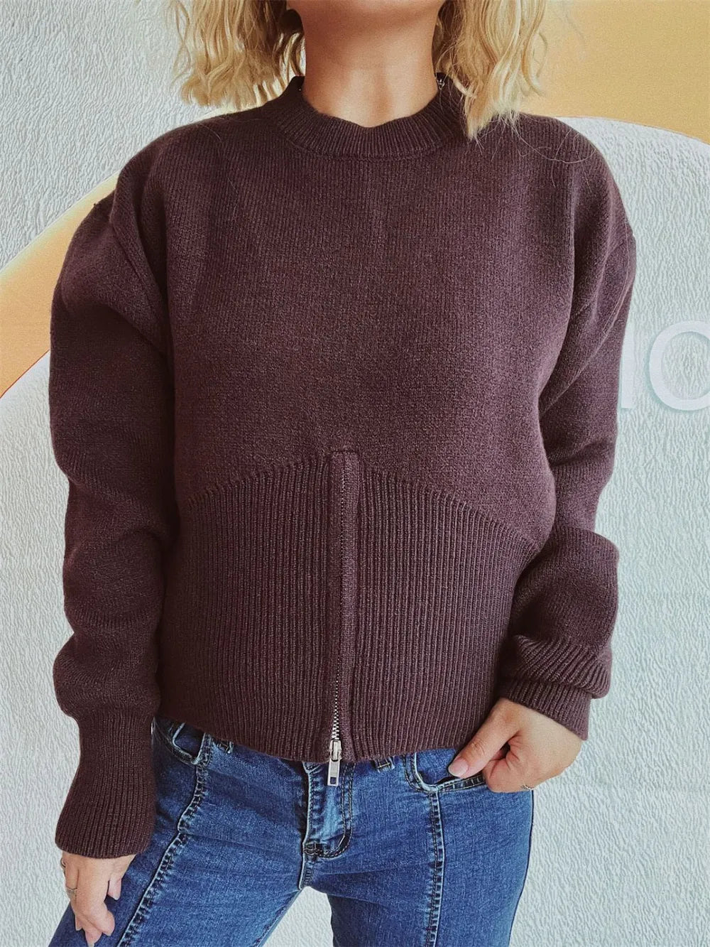Chocolate half-zip knit sweater worn with jeans, hand on hip.