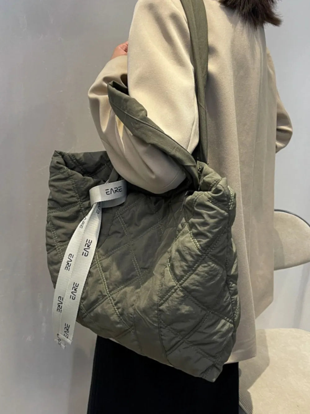 Side view of the olive green quilted tote worn on a shoulder.