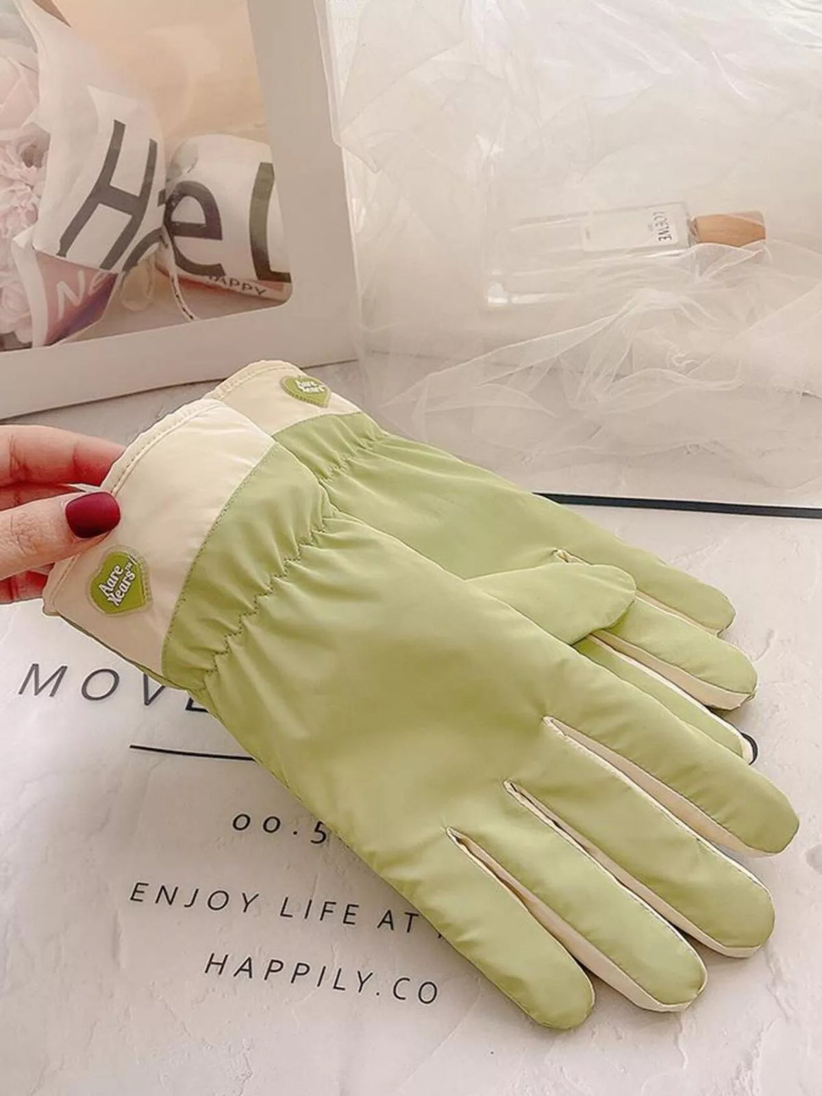 Hand holding the cream cuff of a light green glove to show the gathered wrist.