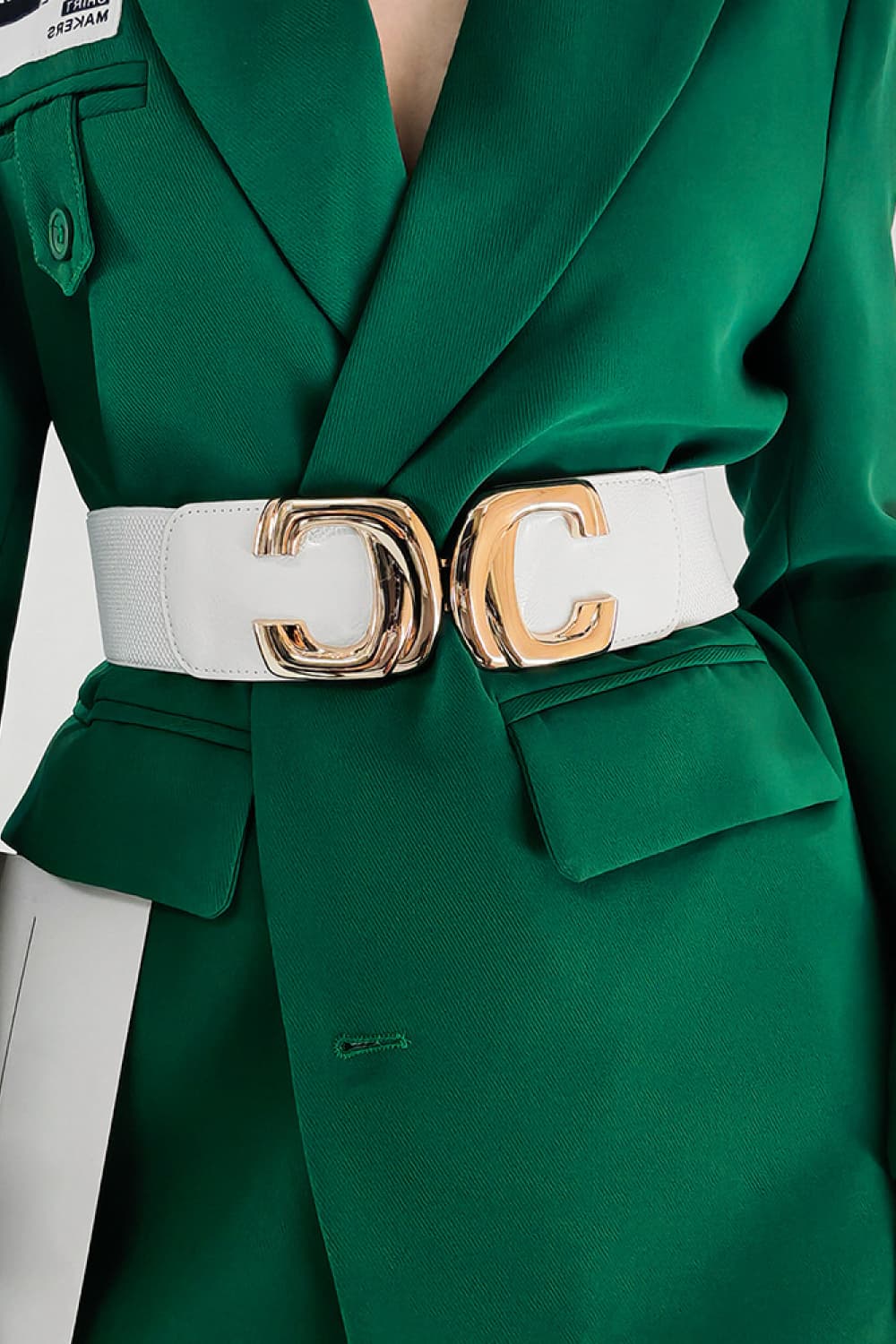 White wide waist belt with a gold-tone buckle, worn over a green blazer.