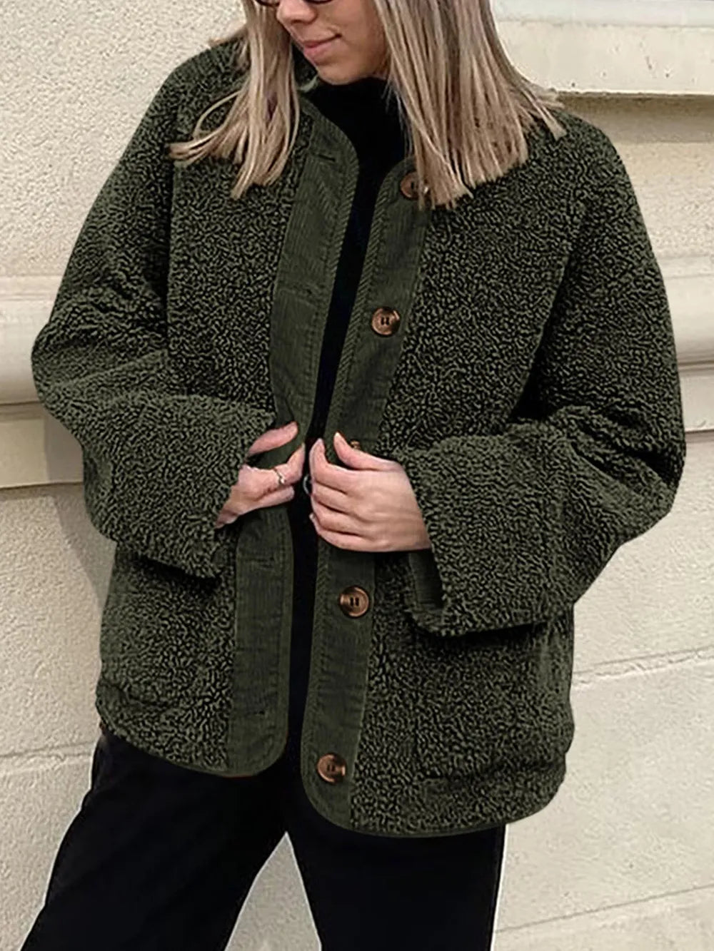 Olive green textured jacket held open over a black top and trousers.