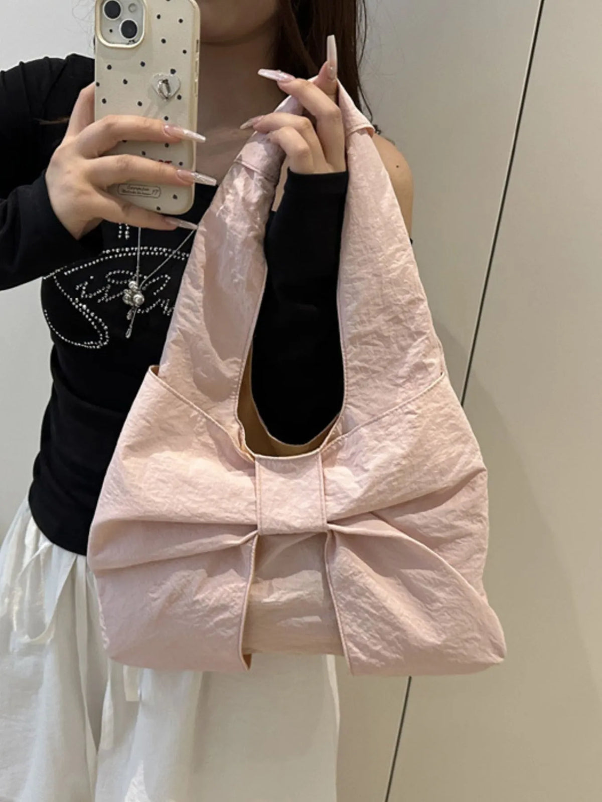 Pale pink bow bag held by its shoulder strap in a mirror view with a black top.