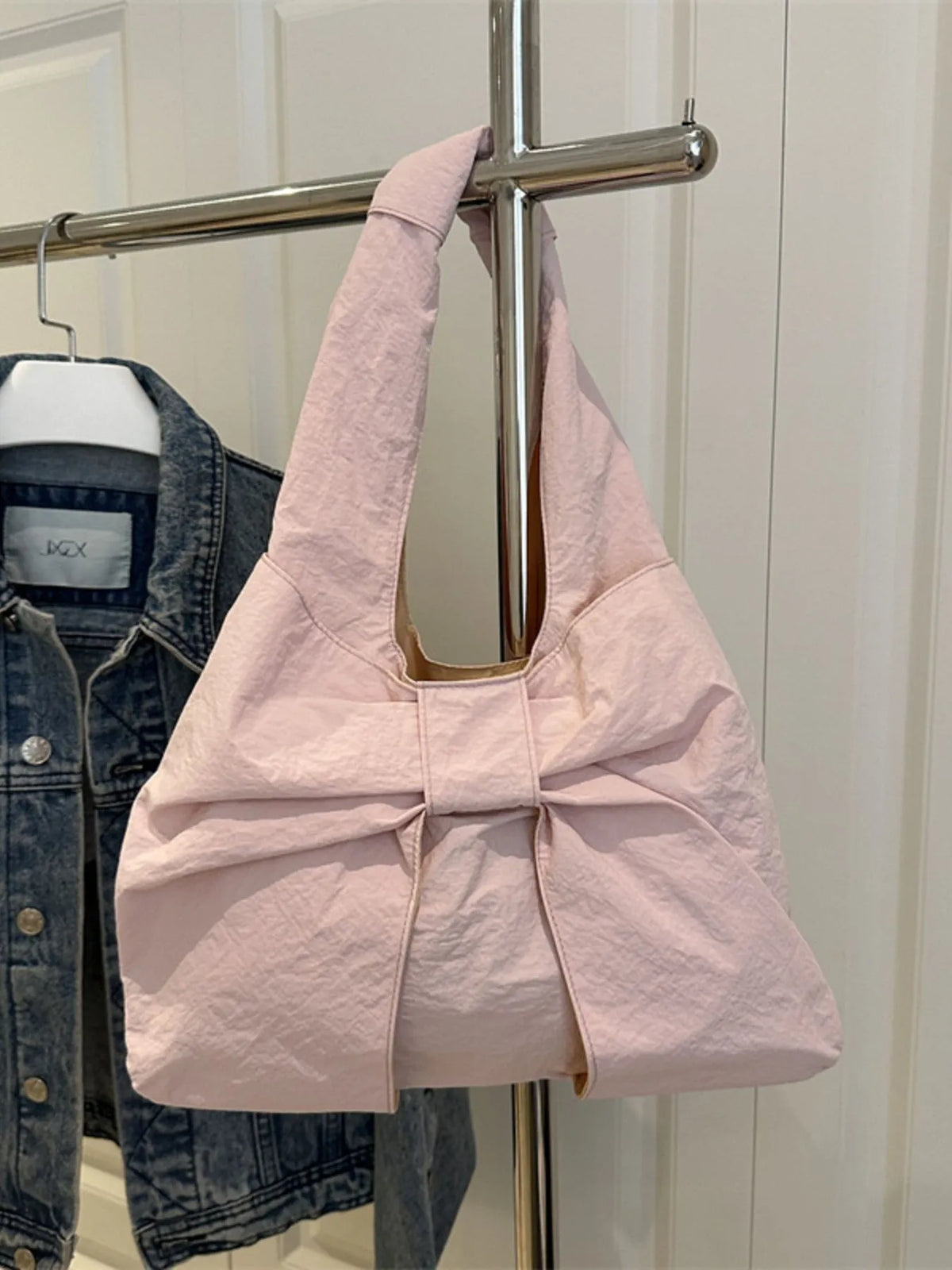 Pale pink bow shoulder bag hanging from a metal rail.
