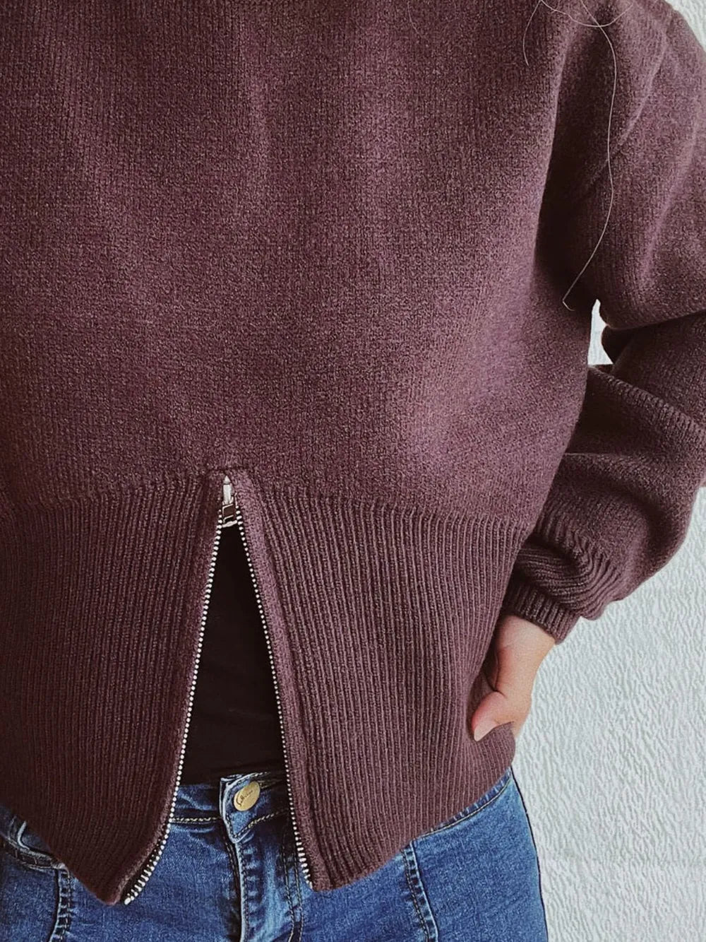 Close-up of the Chocolate sweater's front zip opened into a slit at the ribbed hem.