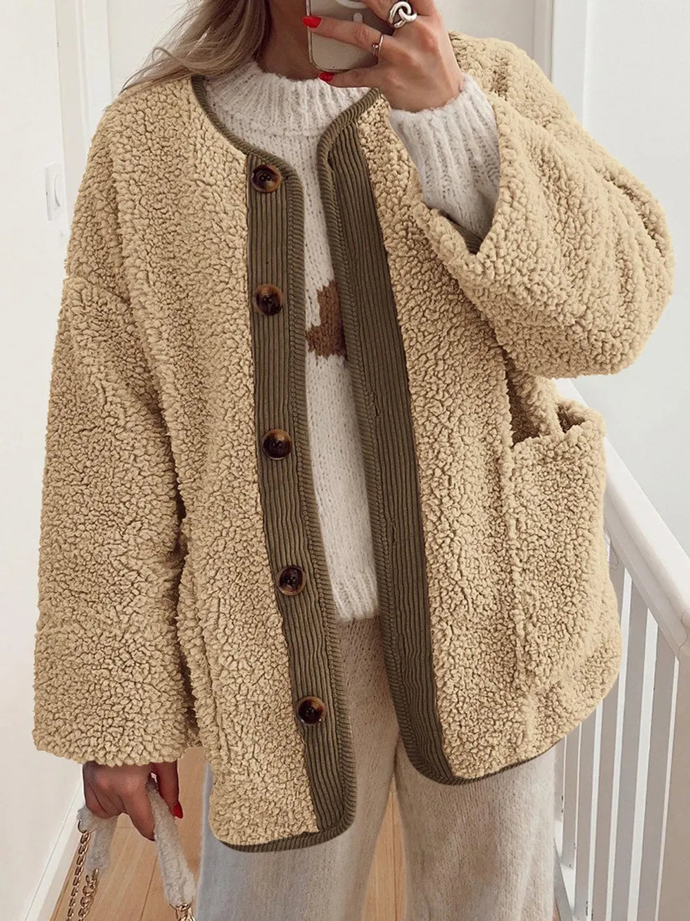 Tan textured jacket with brown contrast trim, worn over a cream sweater.