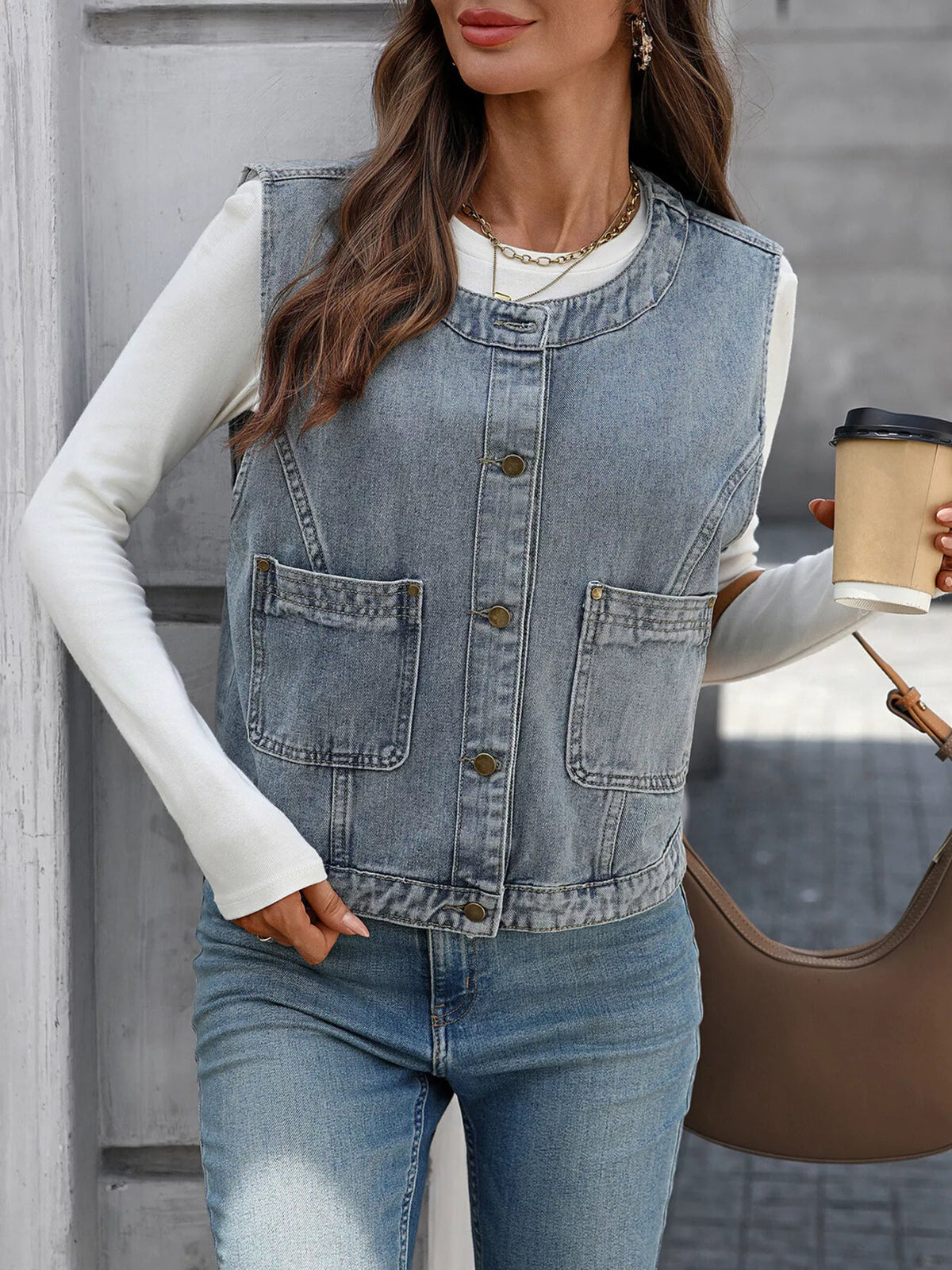 Light-blue denim-look vest buttoned over a white top, shown with a coffee cup and brown bag.