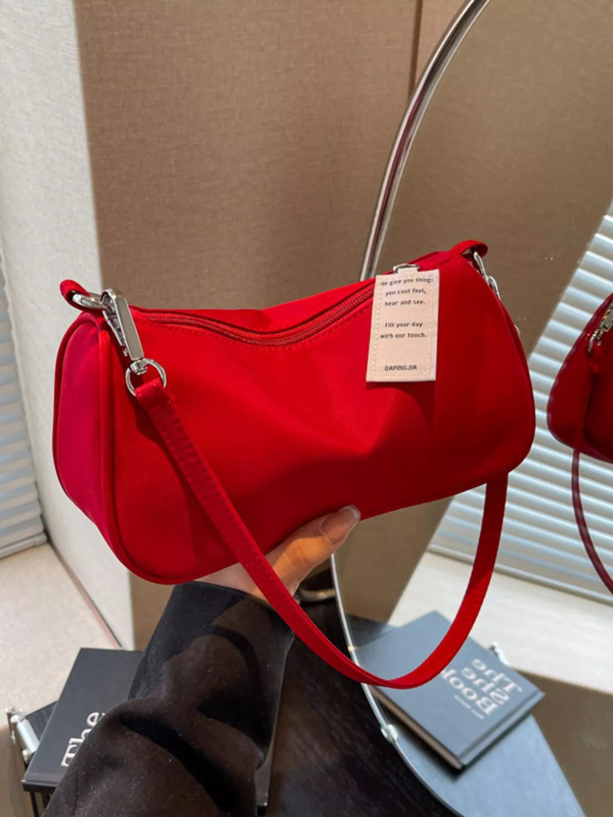 Red crossbody bag held by its short strap against a beige background.