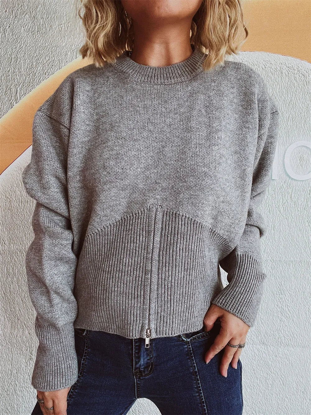 Gray half-zip knit sweater with the front zip closed, worn with hands on hips.
