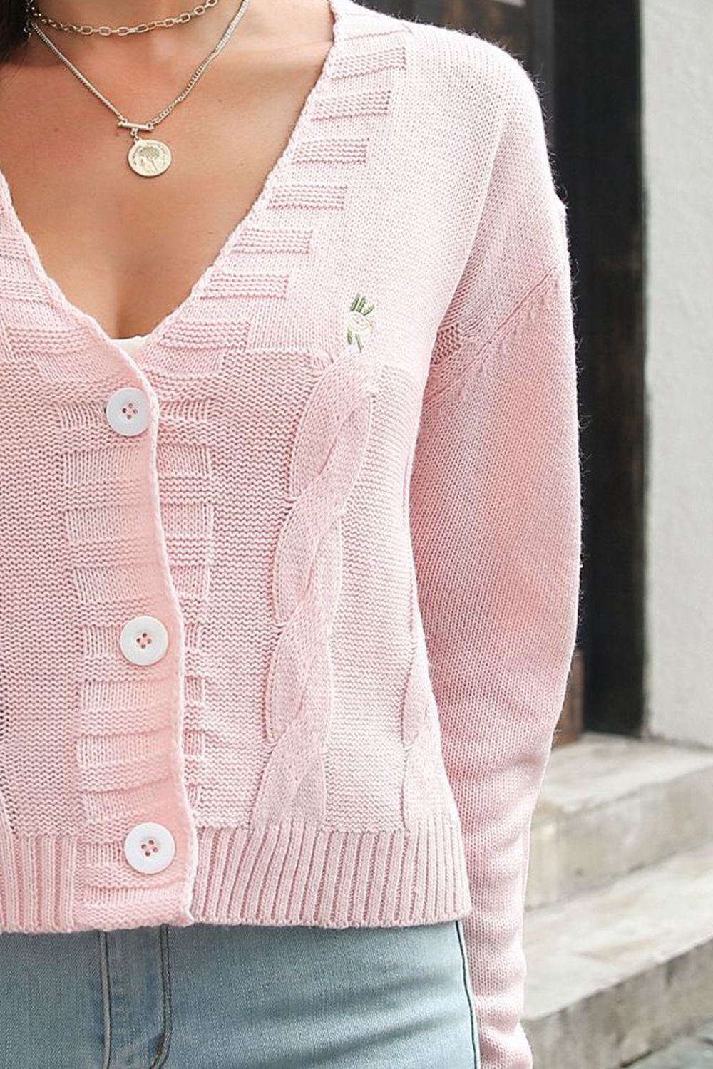 Close-up of the pale pink cardigan's buttons, cable-knit front and ribbed hem.
