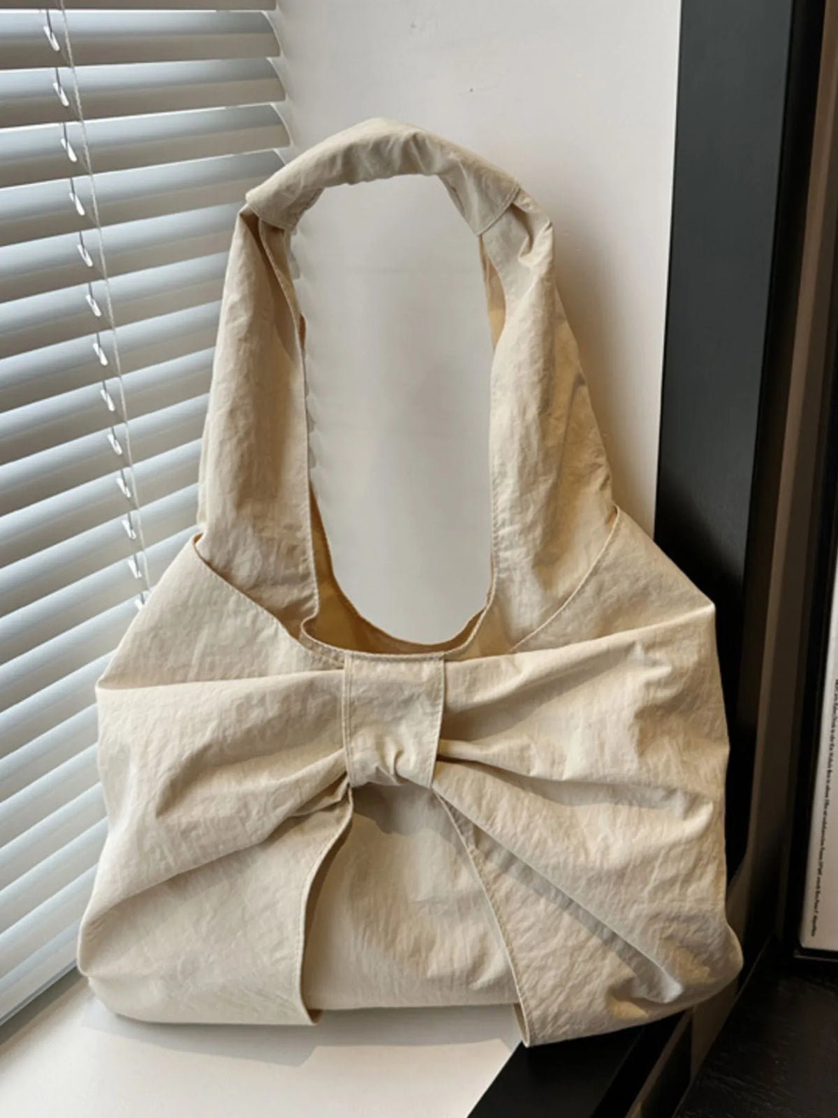 Cream bow shoulder bag standing near a window.