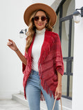 Red open-front knit poncho with fringe, worn with a white top and jeans.
