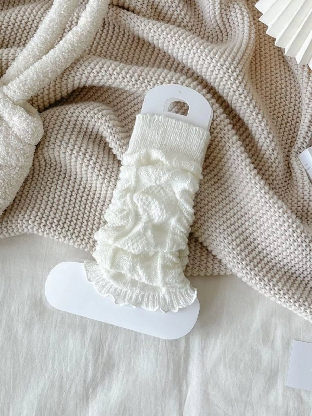 White cable-knit leg warmers gathered on a white display card.