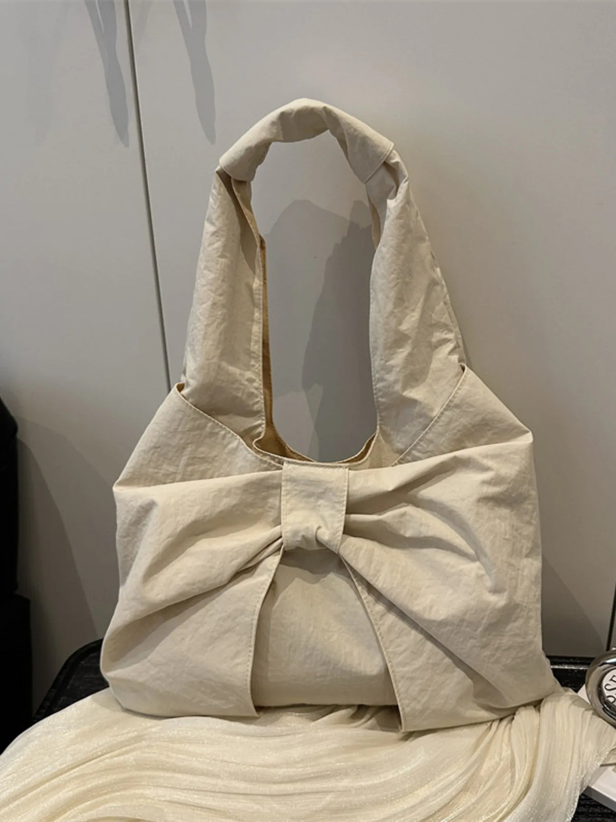 Cream shoulder bag with a large folded bow, resting on a chair.