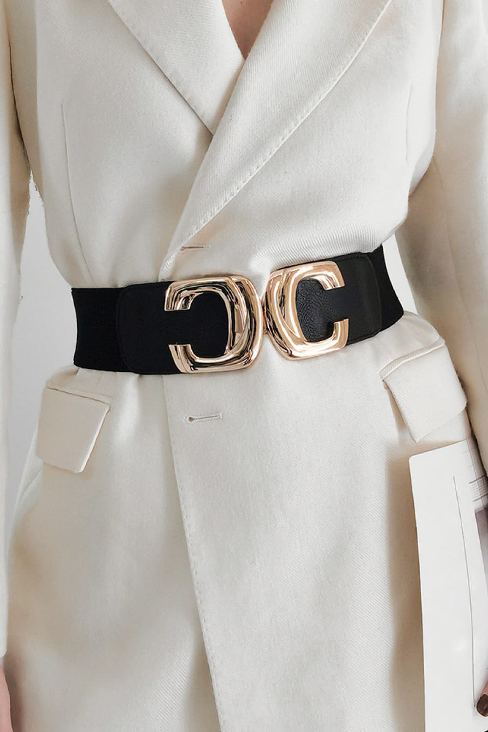 Black wide waist belt with a gold-tone metal buckle, worn over a cream blazer.