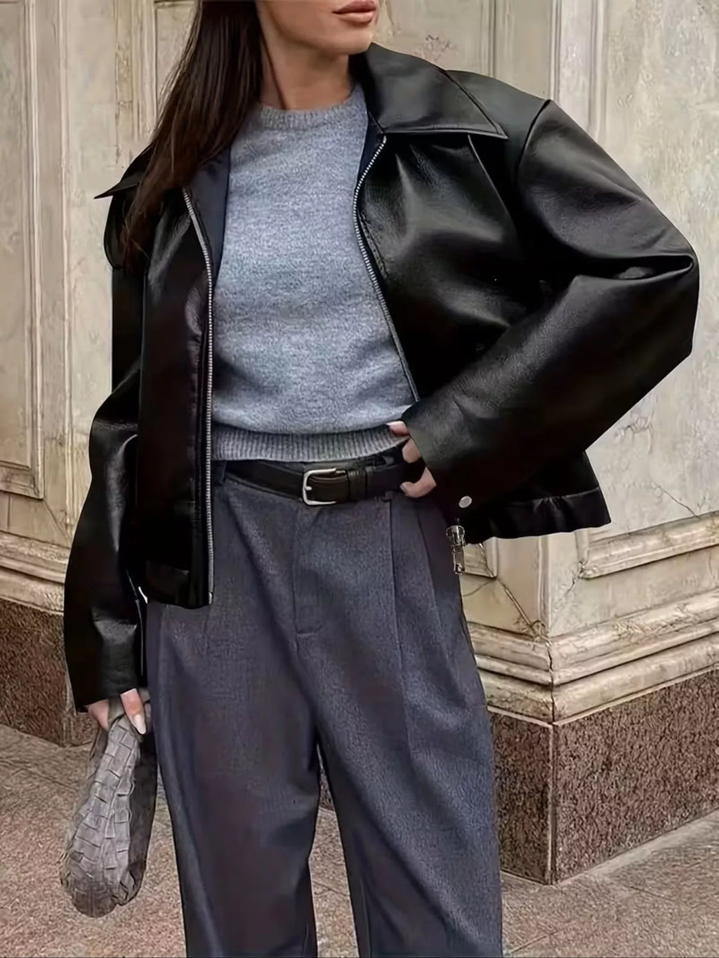 Black faux leather jacket worn over a gray top and gray trousers.