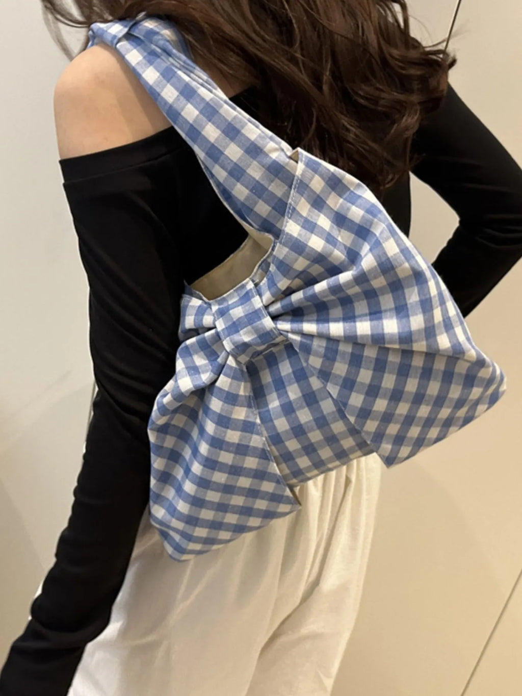 Rear side view of a blue and white checked bow bag worn on the shoulder over a black top.