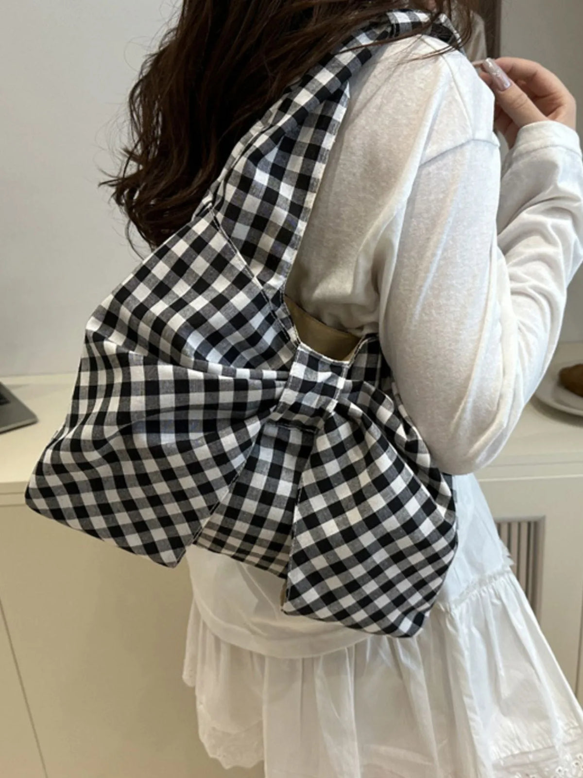 Black and white checked bow bag worn on the shoulder with a light outfit.