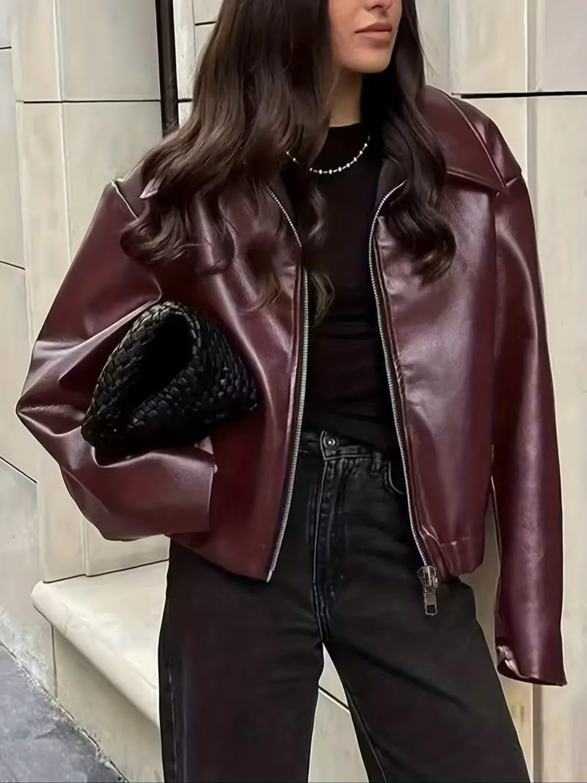 Burgundy faux leather moto jacket worn open with a black top and jeans.