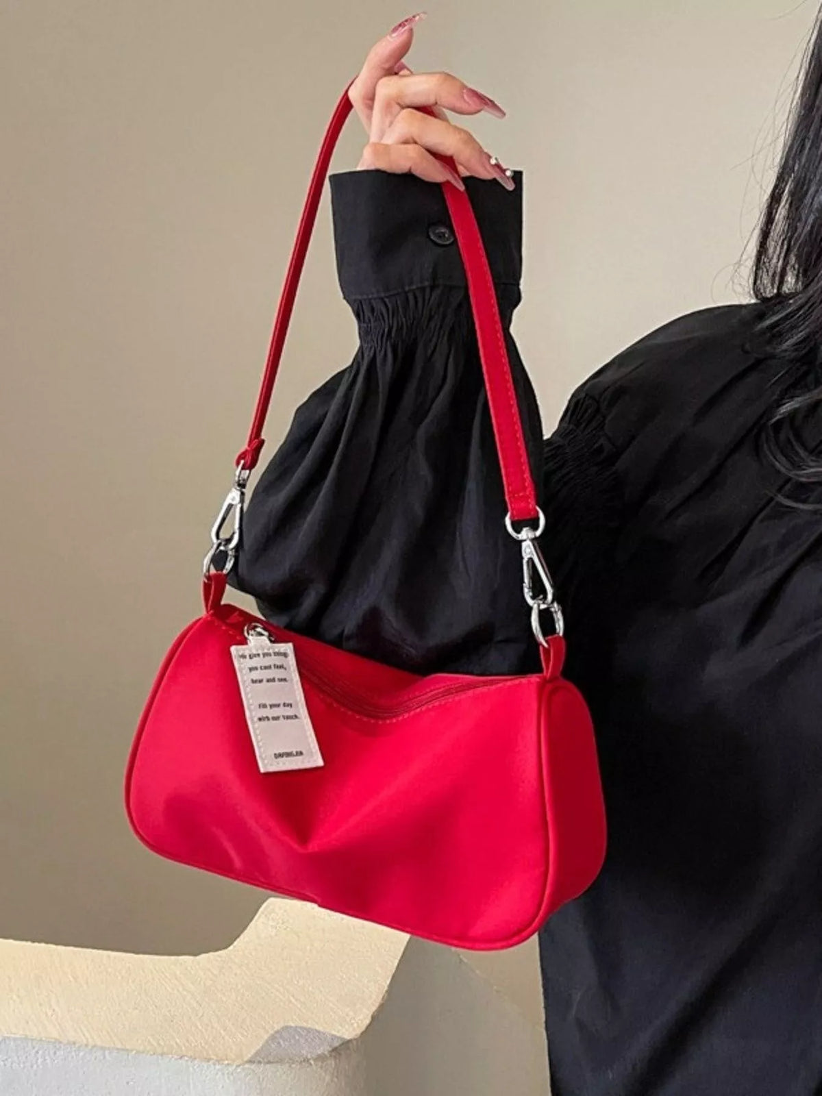 Red crossbody bag held up by its short strap against black clothing.