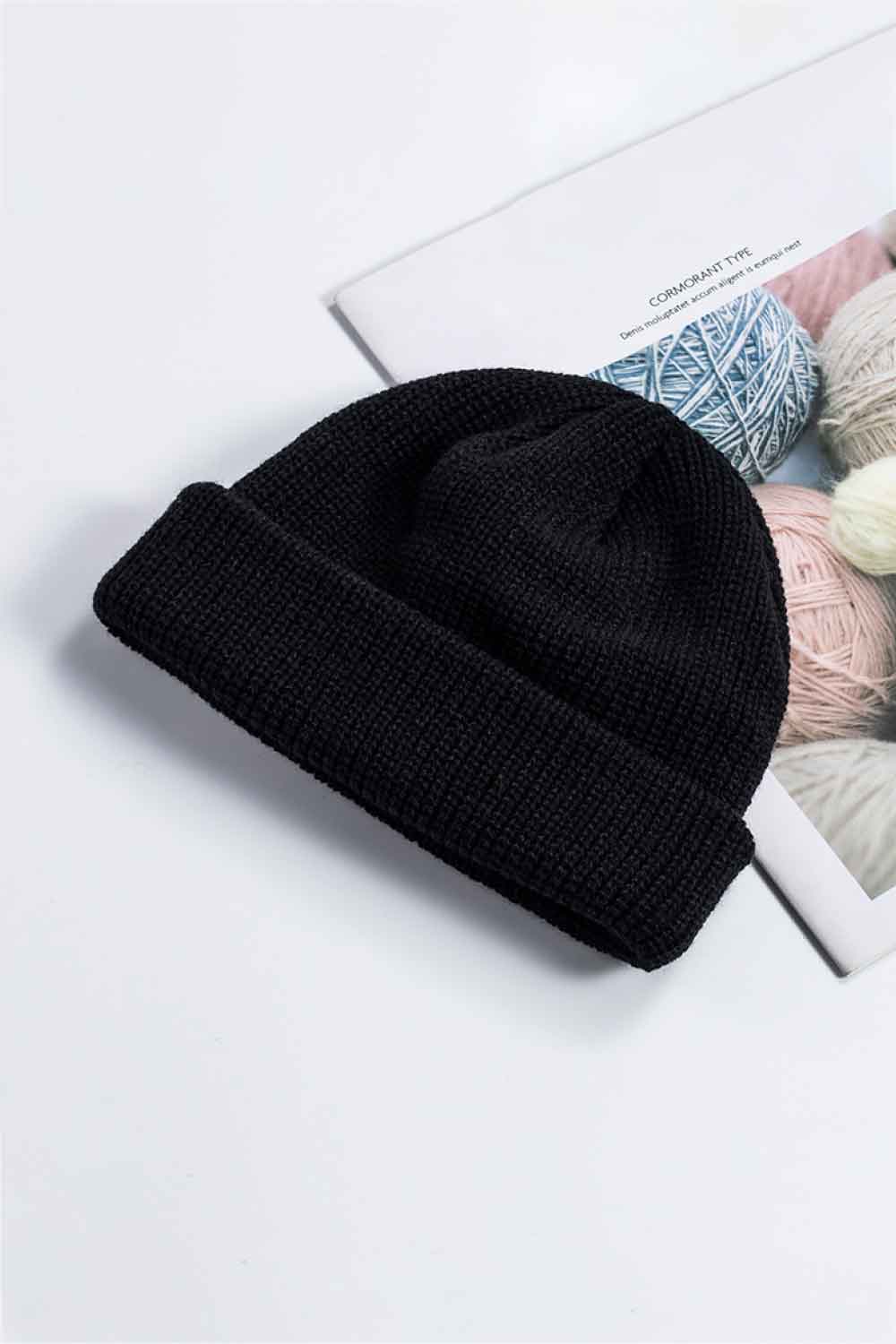 Black knit cuff beanie displayed at an angle on a printed page.