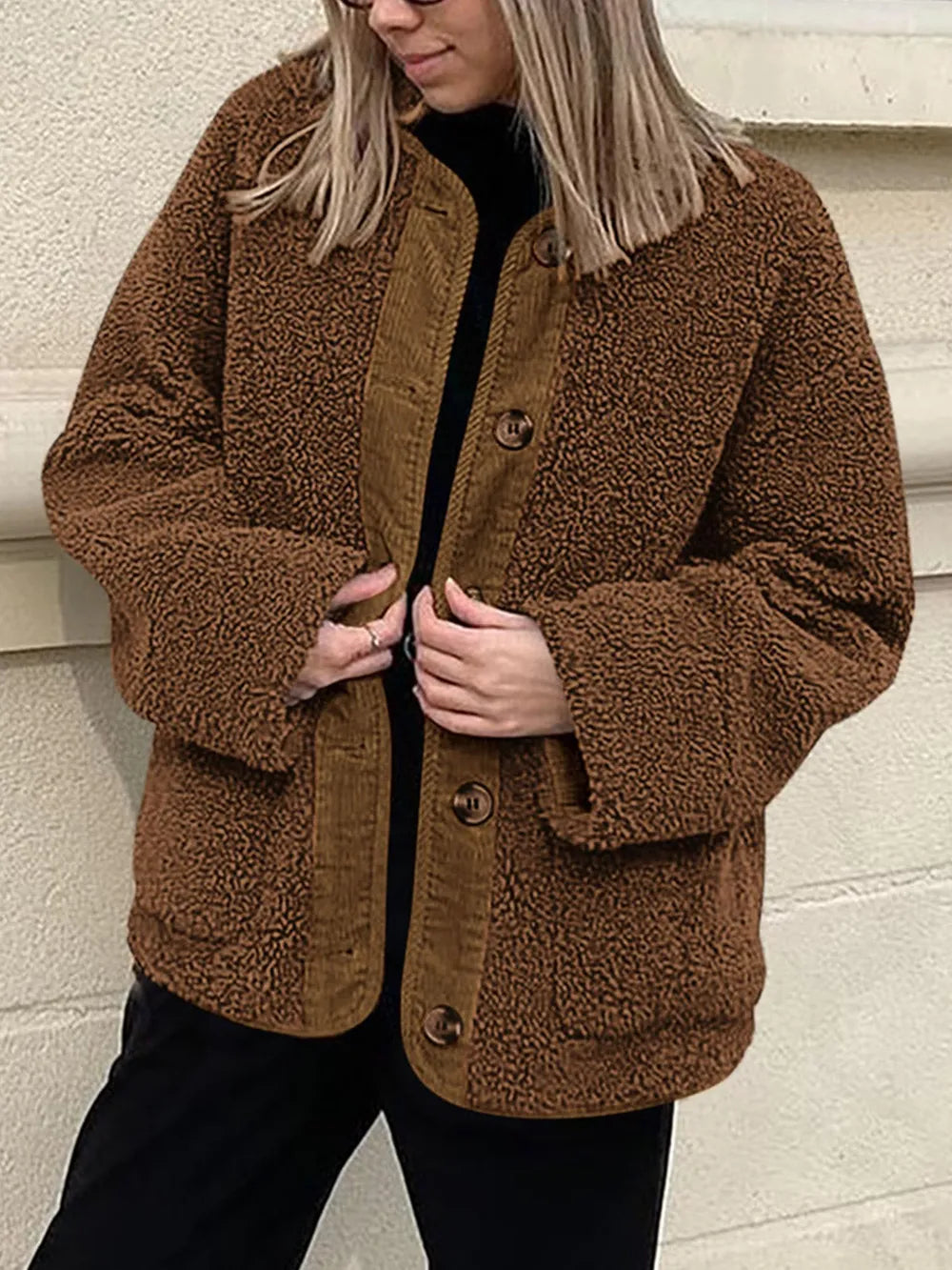Brown textured jacket held open over a black top and trousers.