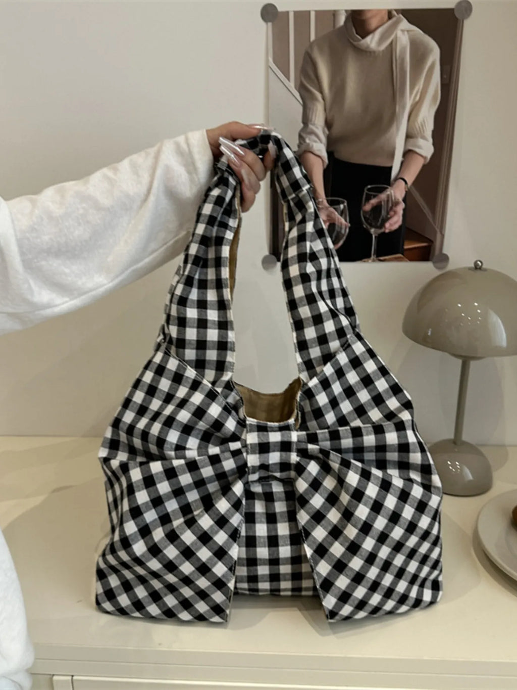 Black and white checked bow bag held by its shoulder strap in a mirror view.