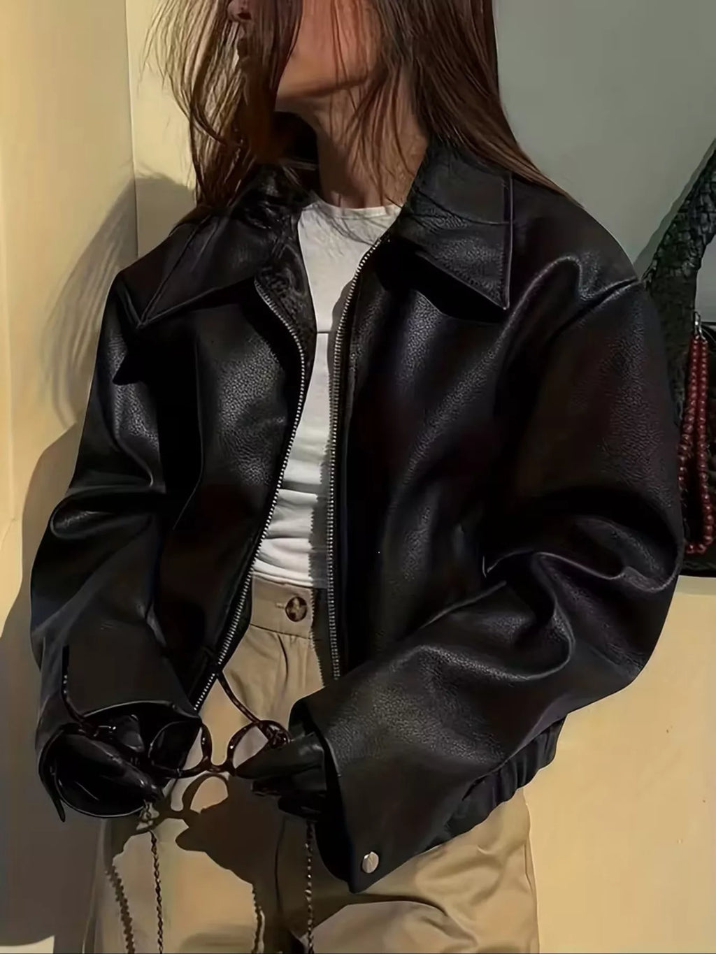 Close front view of the black faux leather jacket with a light top and tan trousers.