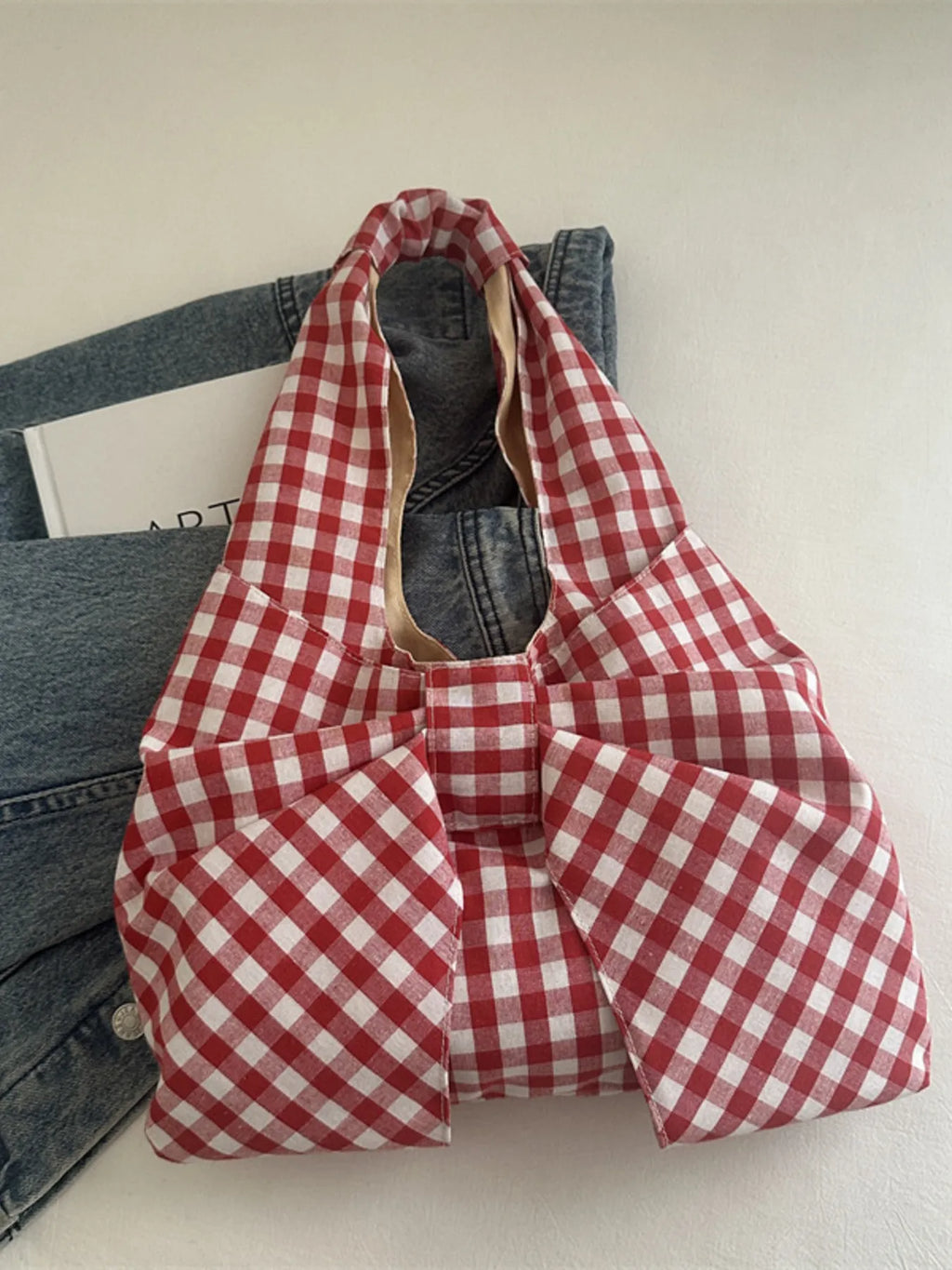 Red and white checked bow shoulder bag resting against denim on a chair.