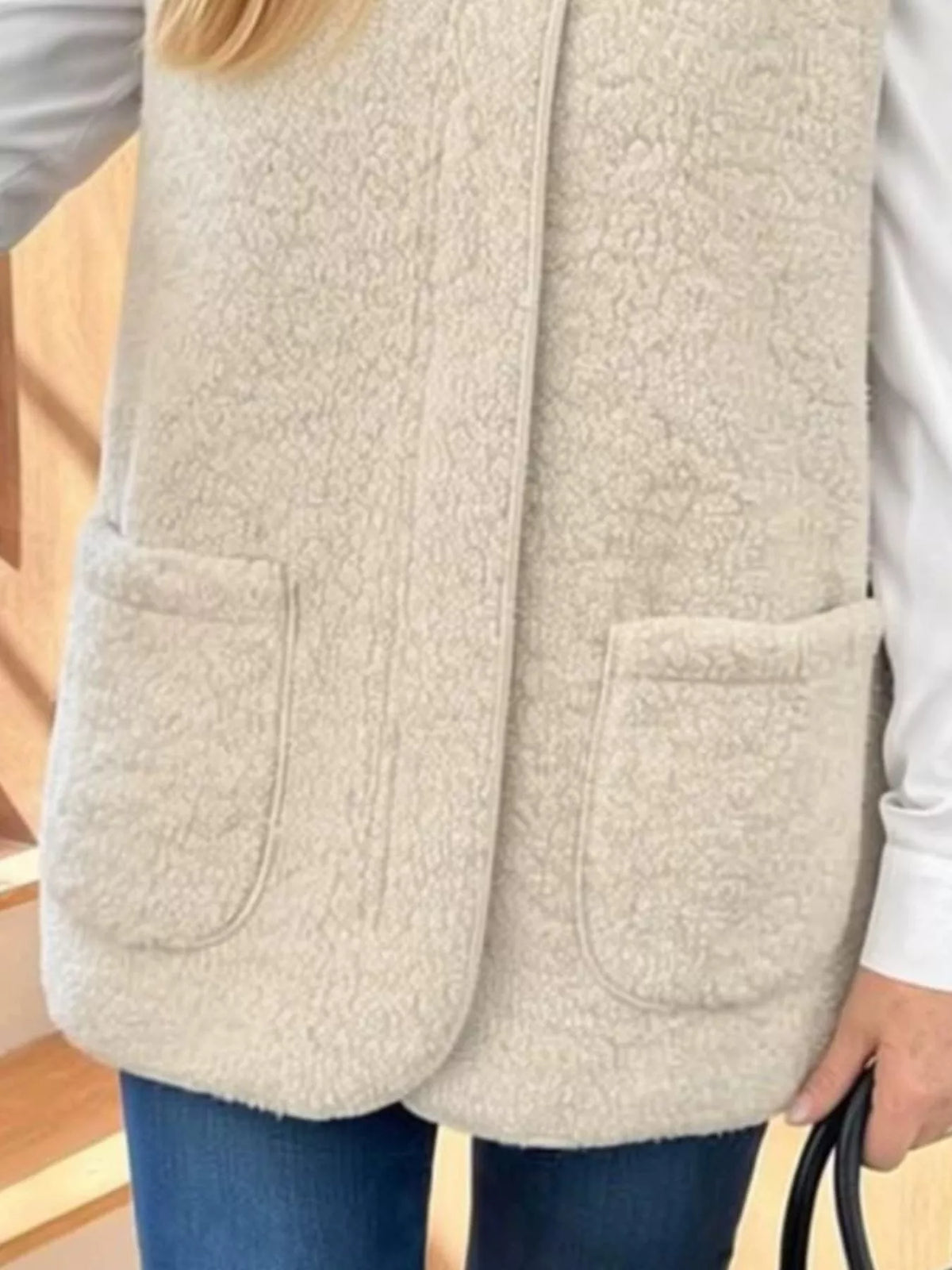 Close view of the beige vest showing its textured fabric, patch pockets and rounded front edges.