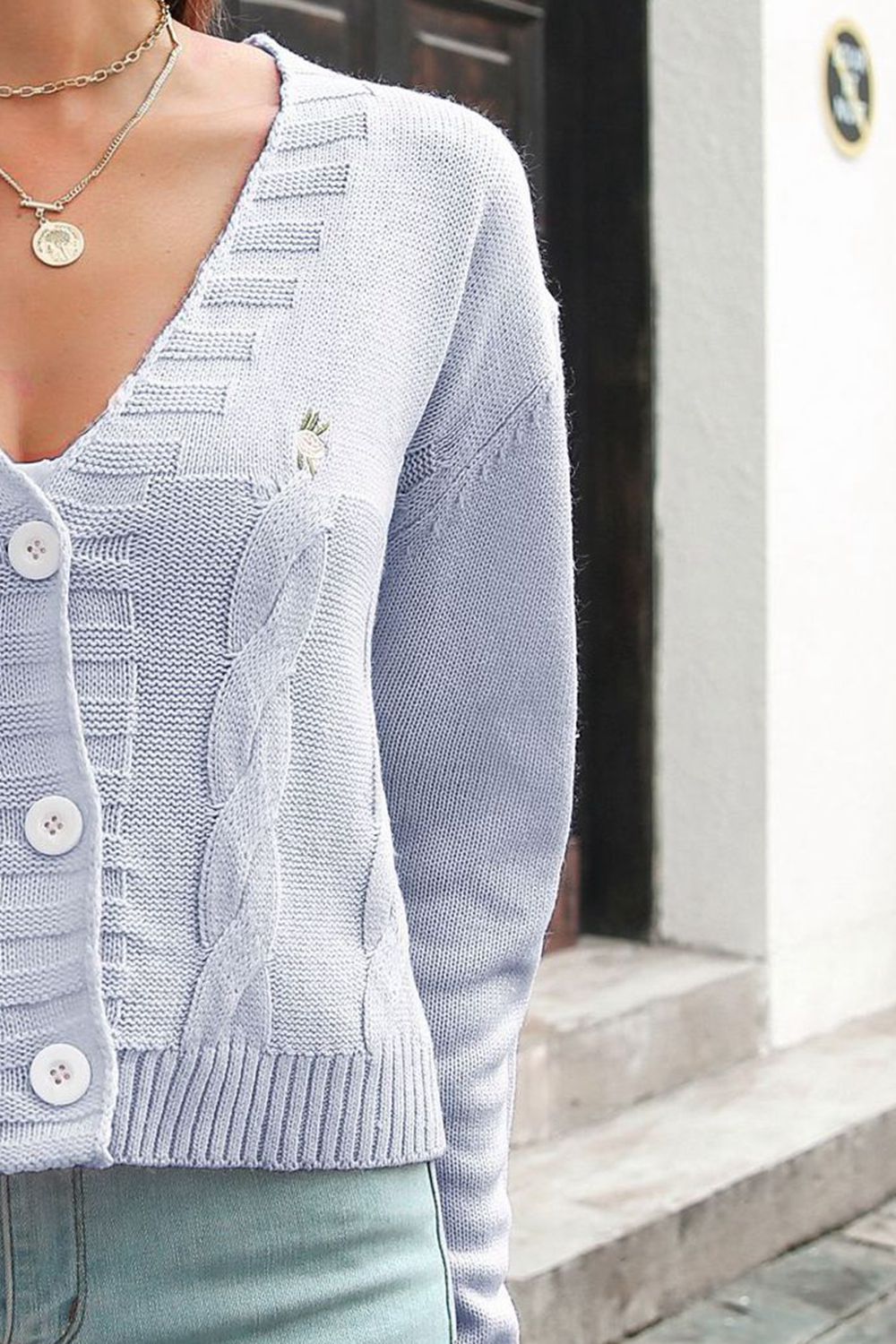Close-up of the light blue cardigan's buttons, cable-knit front and ribbed hem.