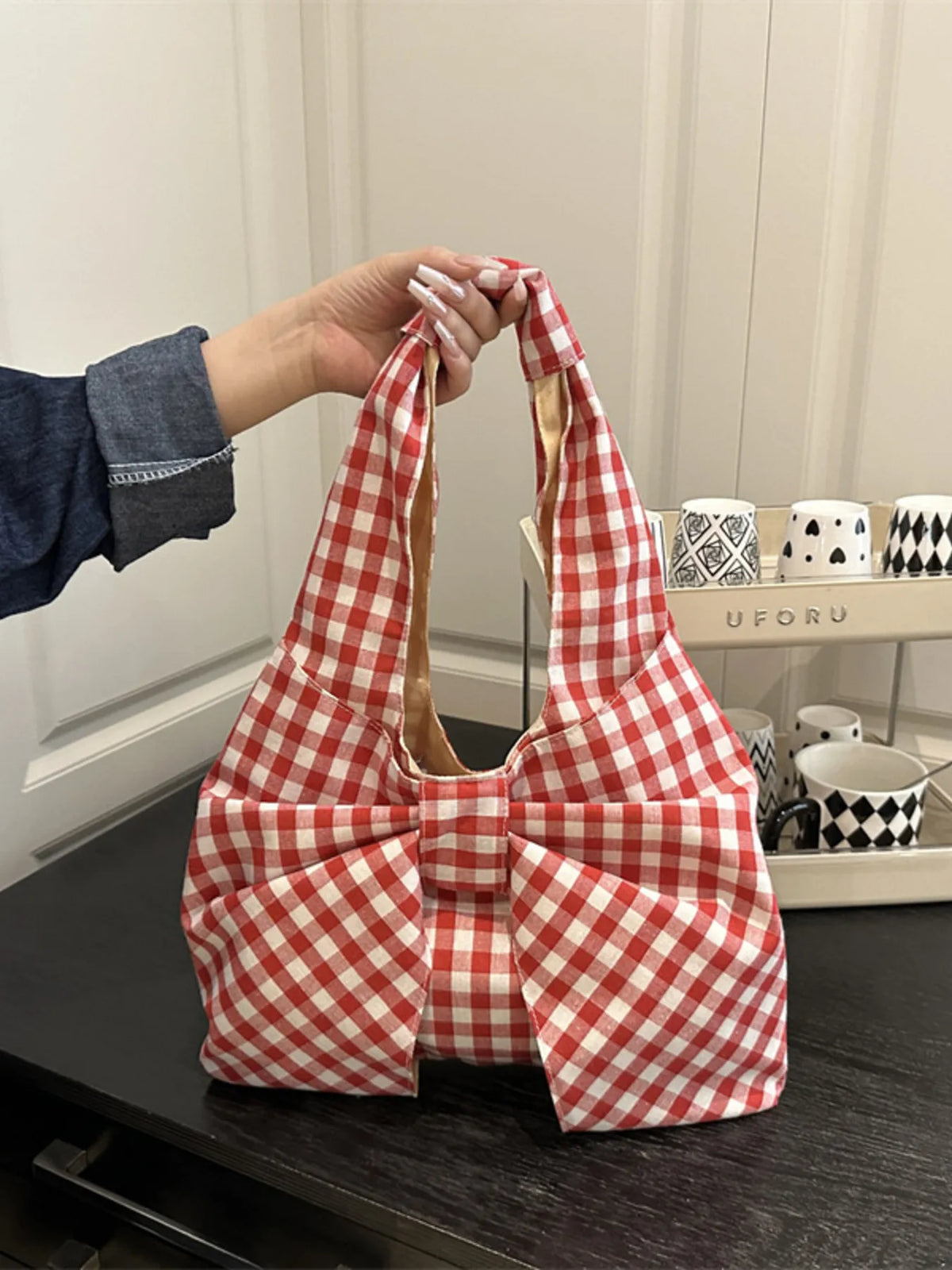 Red and white checked bow bag held by its shoulder strap above a dark table.
