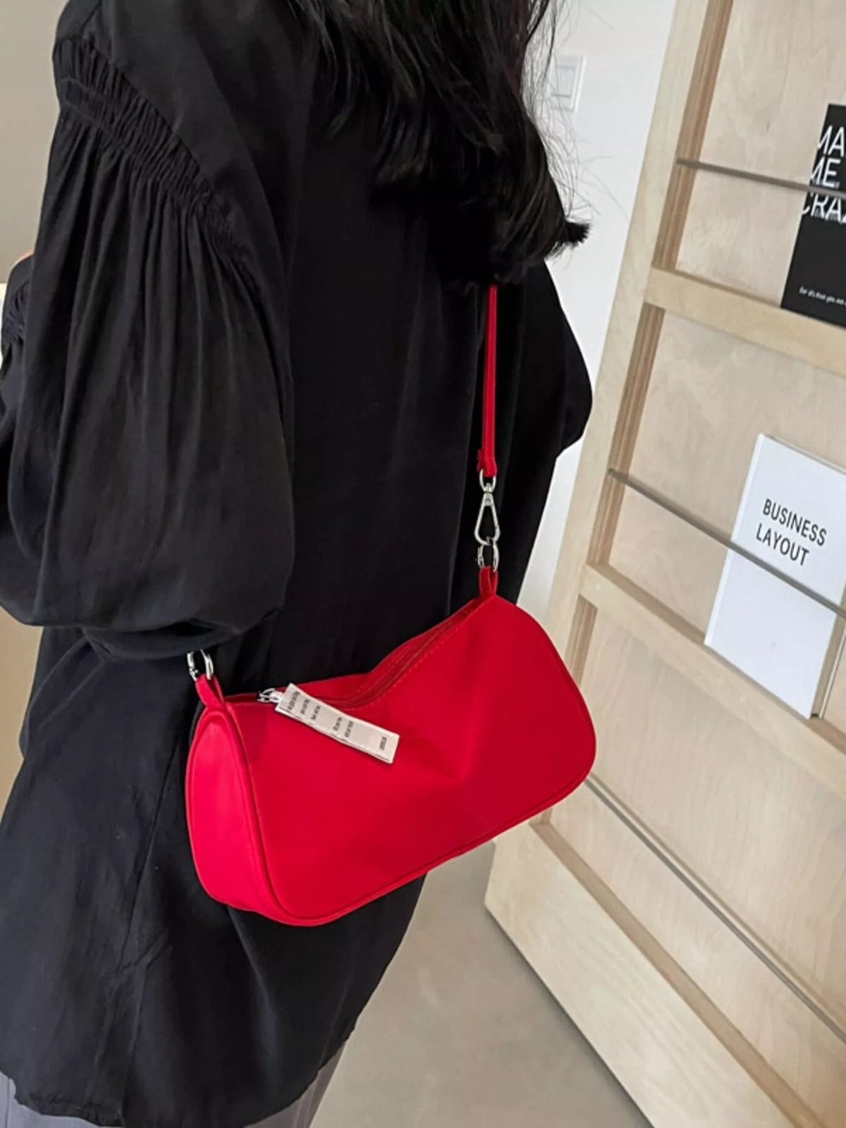Red crossbody bag worn at the side with a black outfit.
