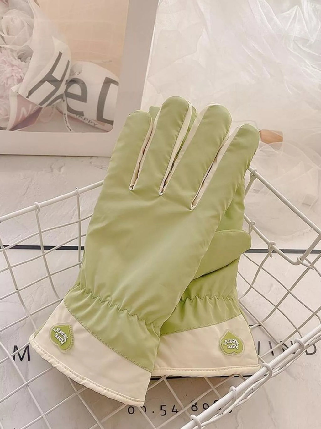 Light green gloves with cream cuffs and small flower accents, laid on a wire tray.