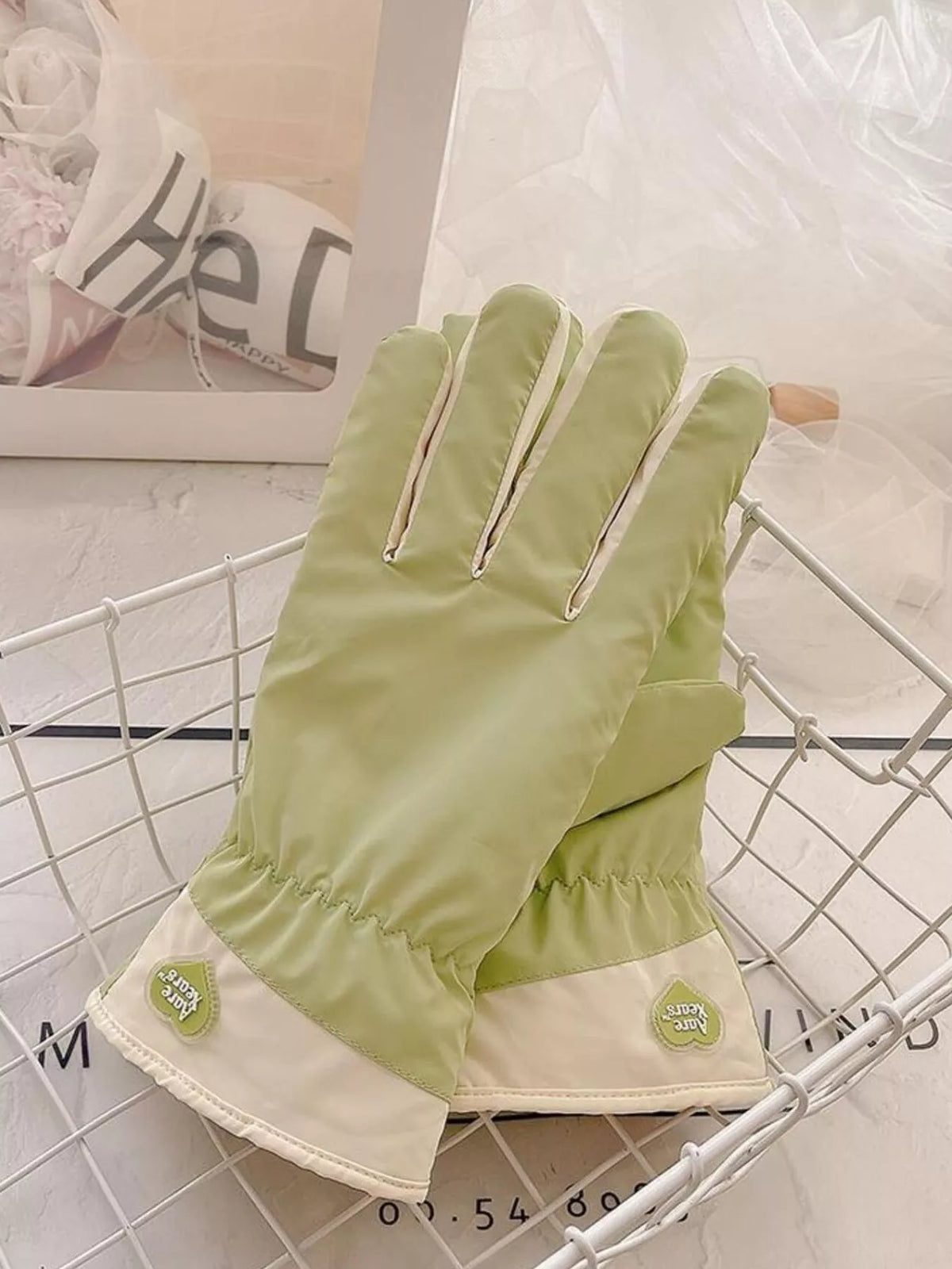 Light green gloves with cream cuffs and small flower accents, laid on a wire tray.