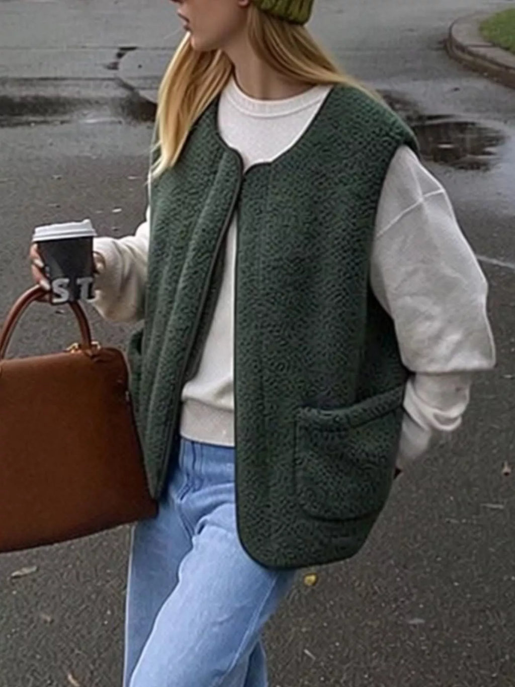 Dark Green sherpa vest worn open over a white sweater, carrying a brown bag outdoors.