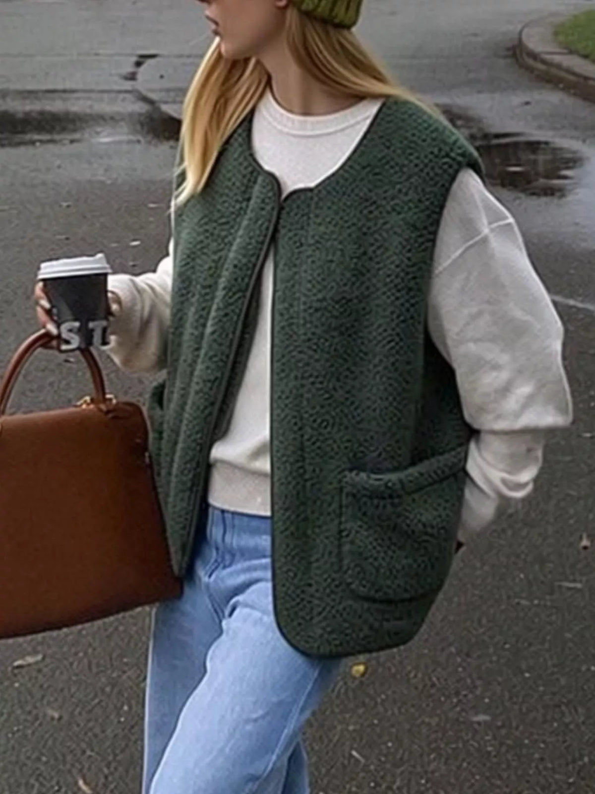 Dark Green sherpa vest worn open over a white sweater, carrying a brown bag outdoors.